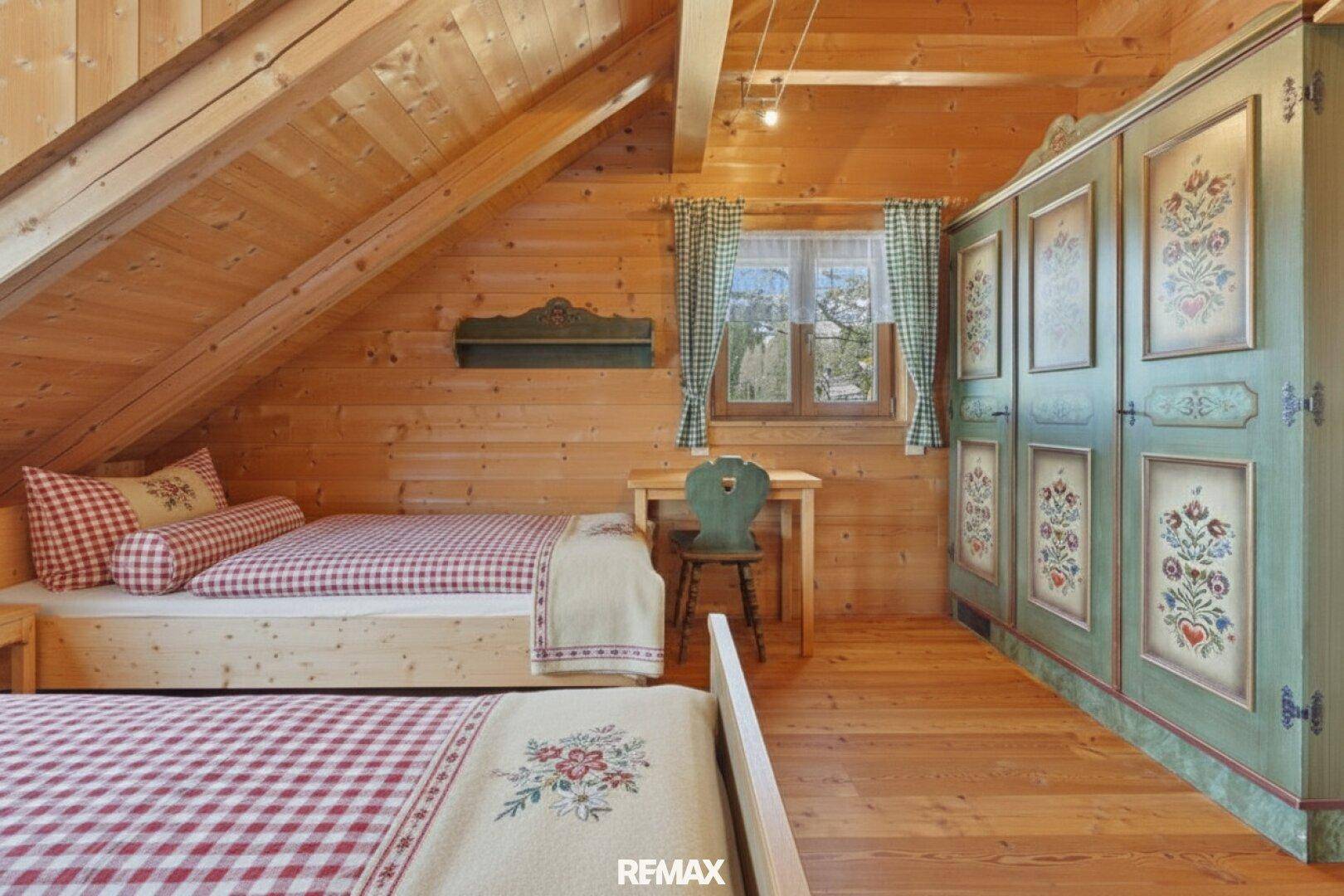 Helles Schlafzimmer mit Holztäfelung, zwei Einzelbetten und einem traditionell bemalten Kleiderschrank.