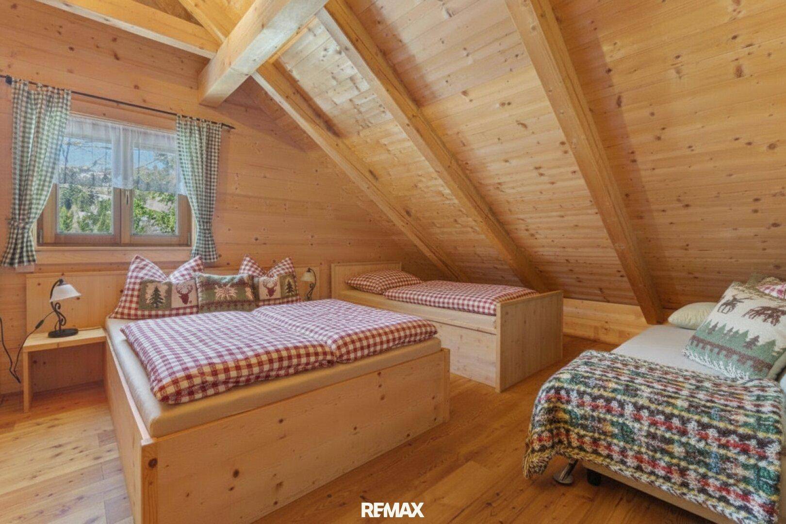 Gemütliches Schlafzimmer im Dachgeschoss mit schrägen Holzdecken, mehreren Betten und karierter Bettwäsche.