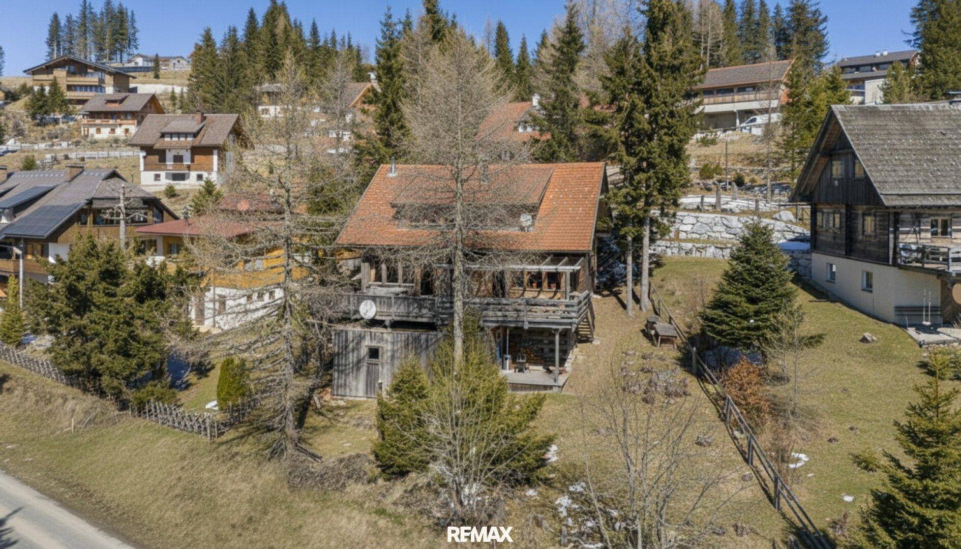 Luftaufnahme eines traditionellen Holzhauses in einer ländlichen Siedlung, umgeben von Bäumen und anderen Gebäuden.