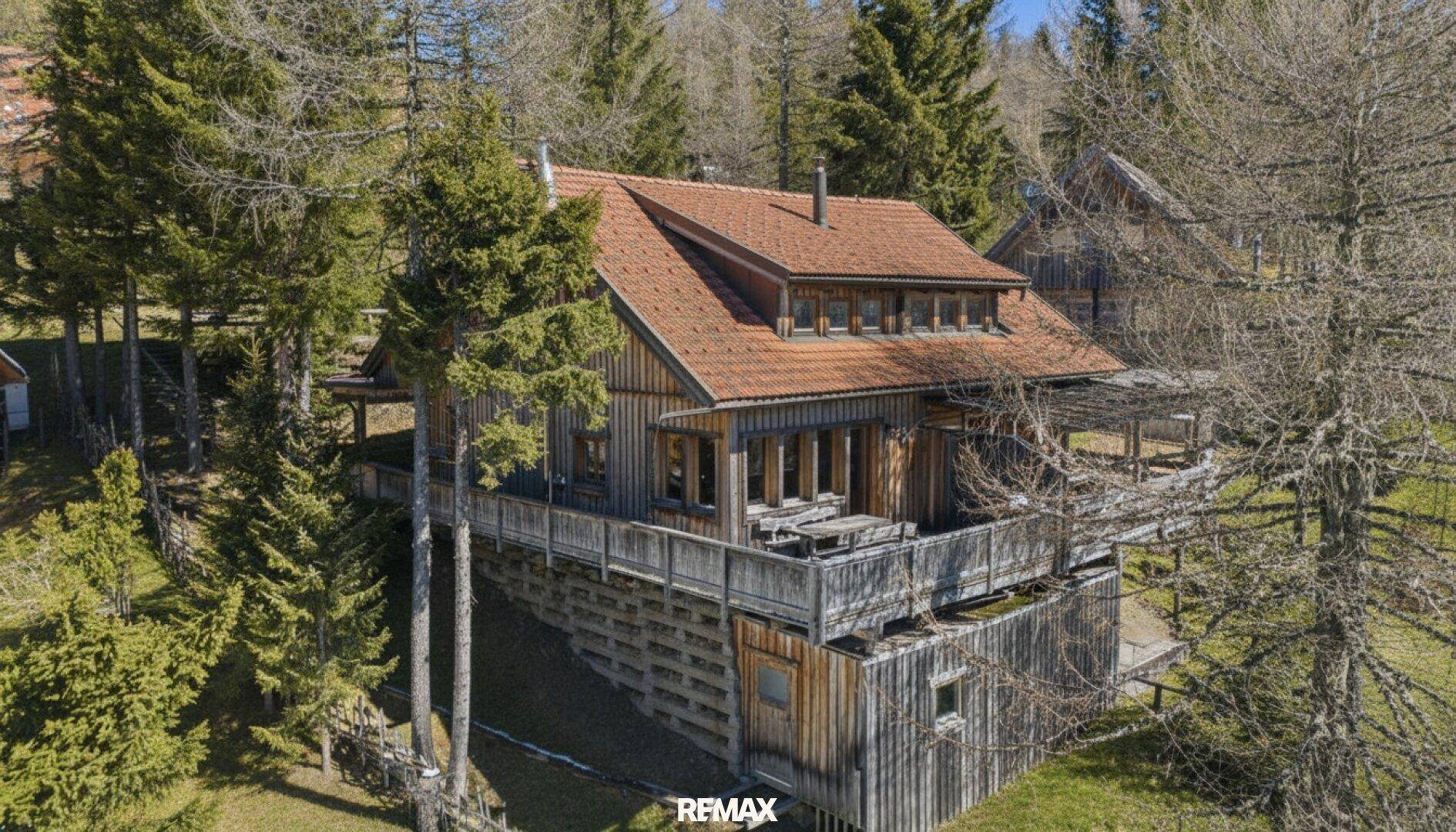 Ansicht des mehrstöckigen Holzhauses mit seinen charakteristischen Balkonen und der umliegenden Waldlandschaft.