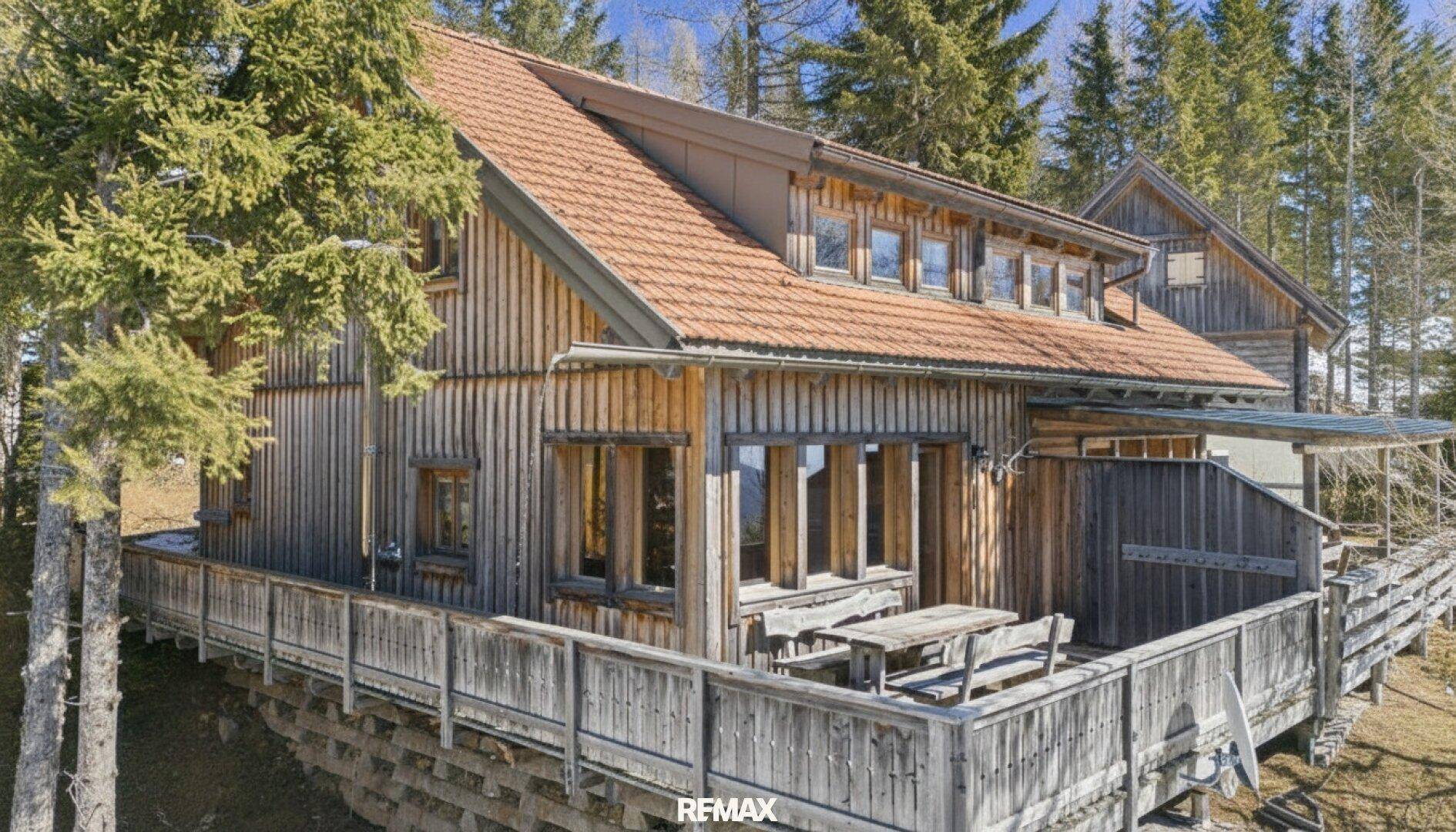 Traditionelles Holzchalet mit großer Holzterrasse und rustikalen Gartenmöbeln, umgeben von Bäumen.