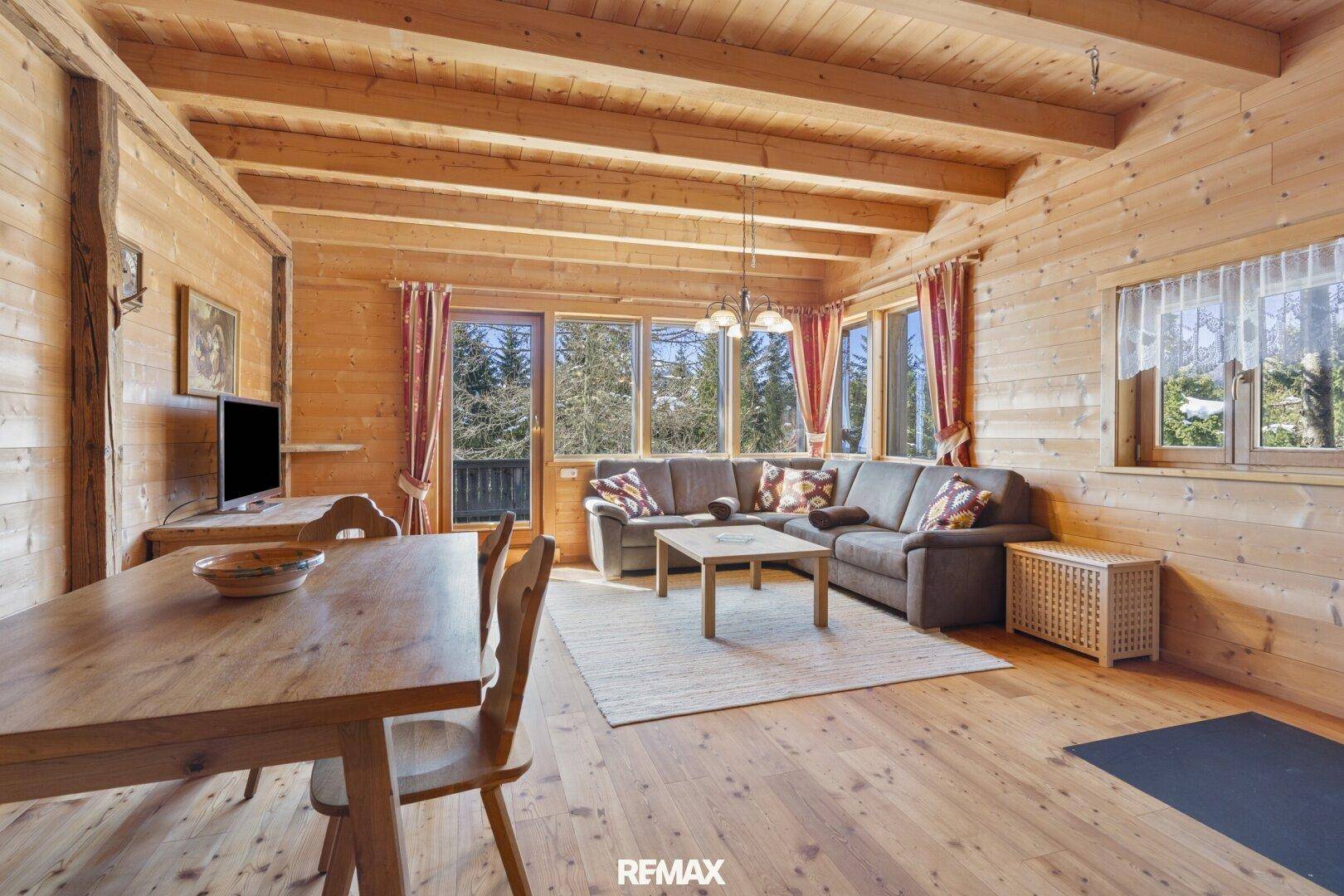 Gemütlicher Wohn-Essbereich im Chalet-Stil mit viel Holz, großen Fenstern und Blick ins Grüne.