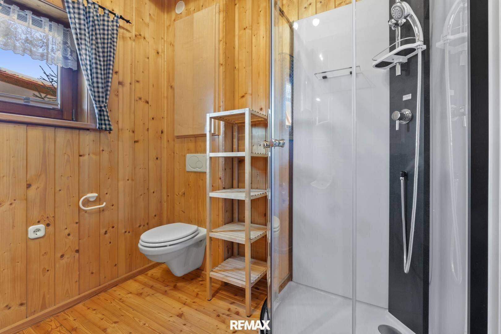 Badezimmer mit Holztäfelung, moderner Duschkabine und wandhängendem WC.