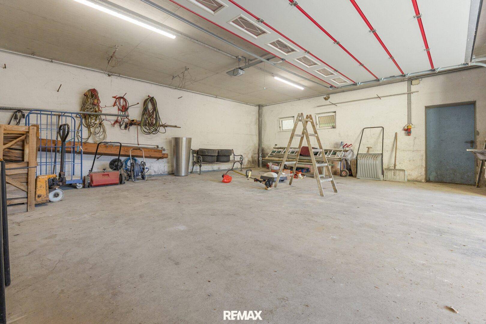 Geräumige Garage oder Werkstatt mit Betonboden und verschiedenen Werkzeugen und Geräten.