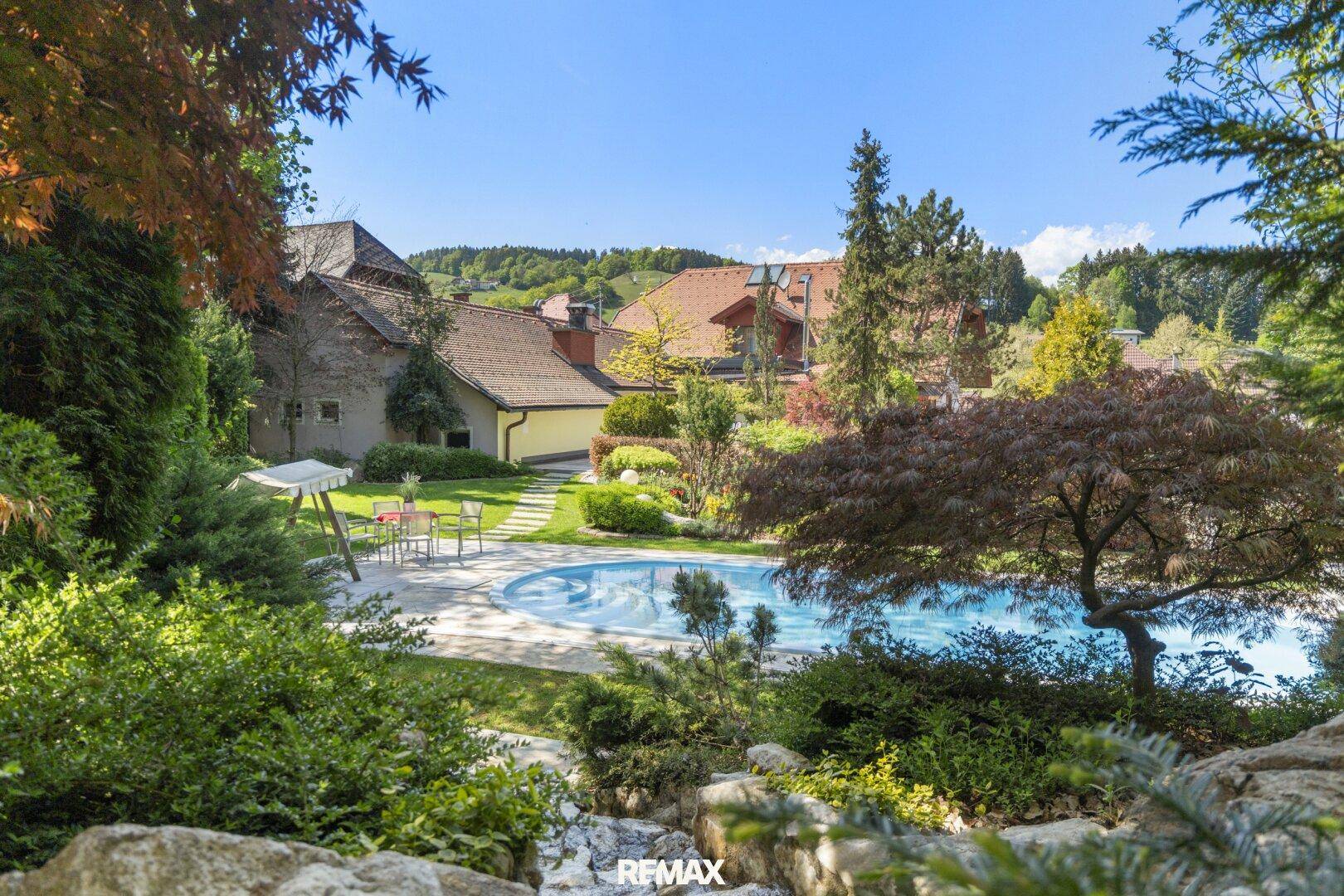 Idyllischer Gartenbereich mit großem Swimmingpool, umgeben von üppigem Grün und Bäumen.
