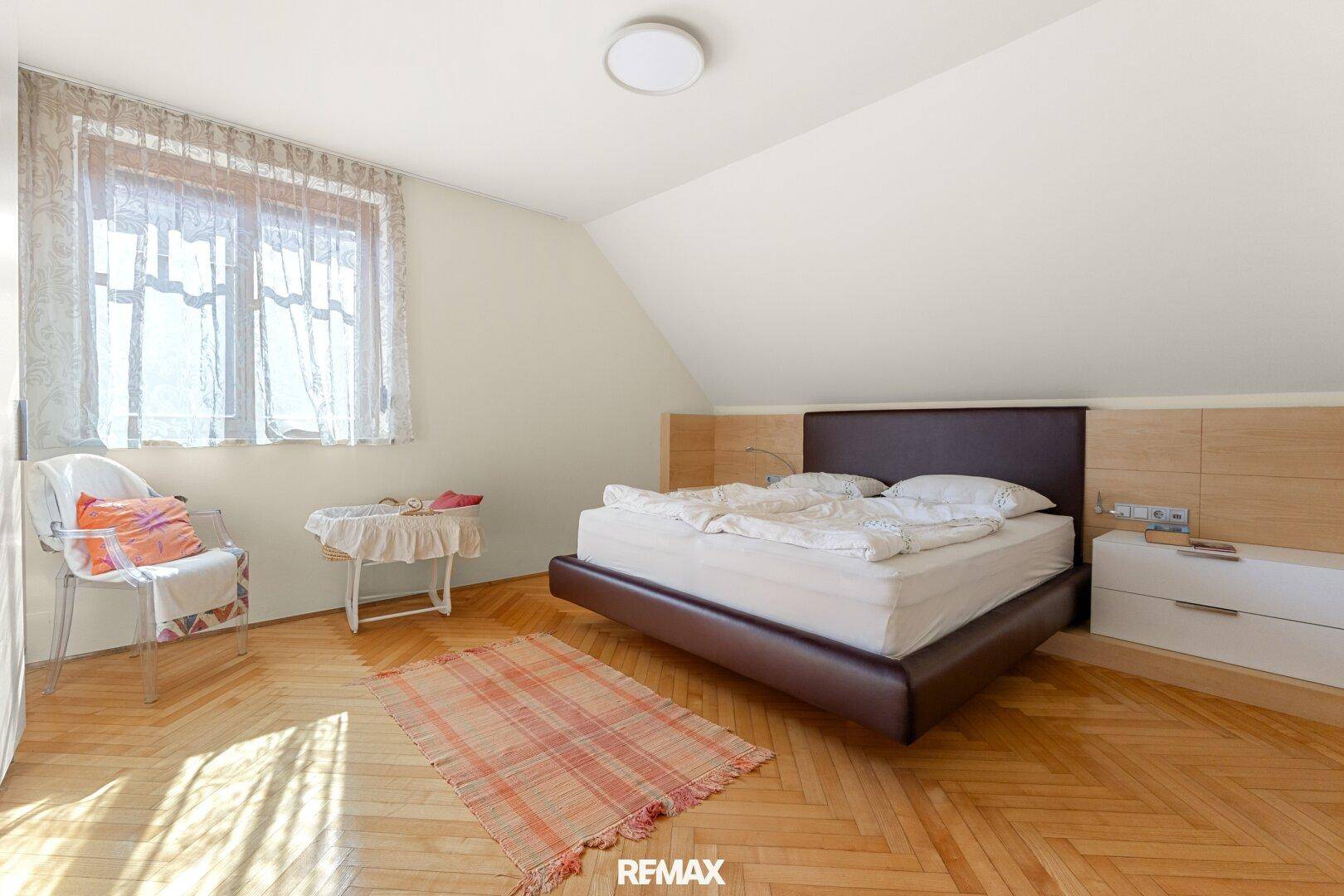 Ruhiges Schlafzimmer im Dachgeschoss mit Parkettboden, schräger Decke und großem Fenster.