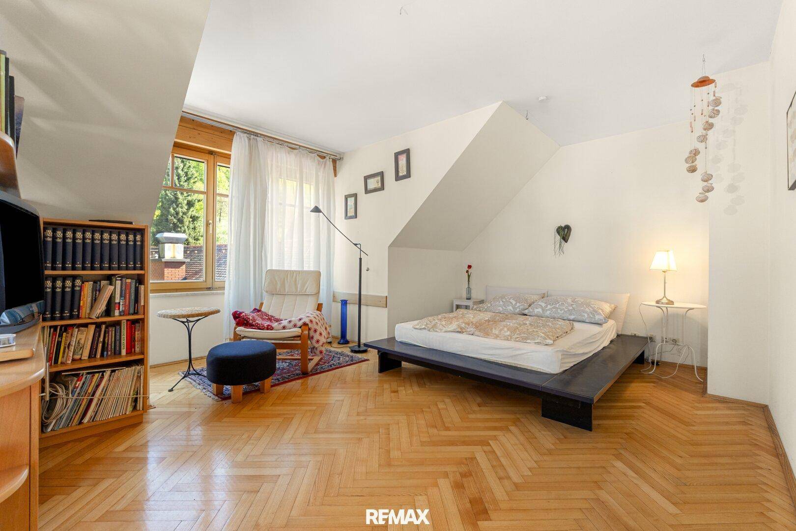 Gemütliches Schlafzimmer im Dachgeschoss mit Parkettboden, Bücherregal und viel natürlichem Licht.