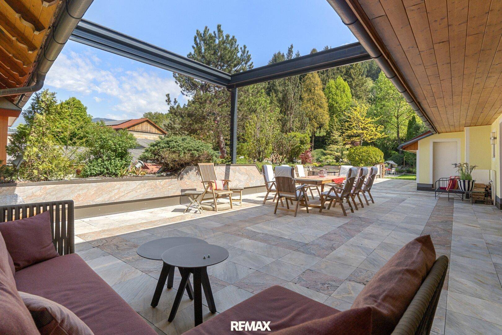 Weitläufige Terrasse mit überdachtem Essbereich und bequemen Lounge-Möbeln, umgeben von Grün.