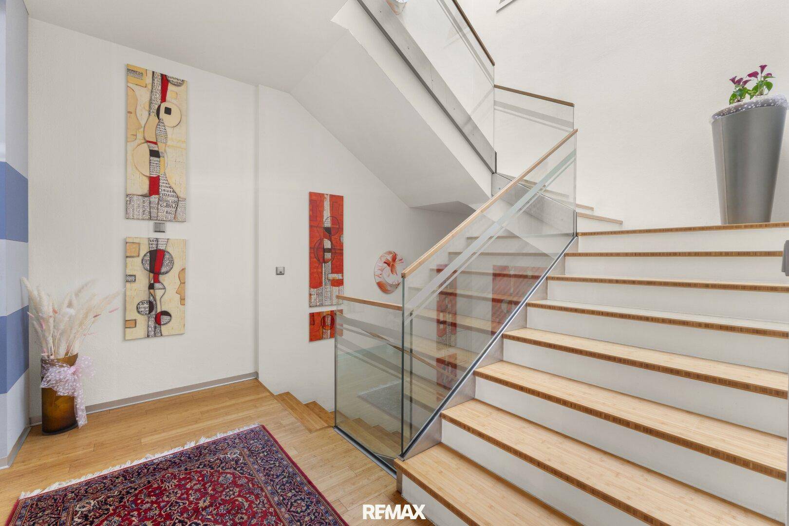 Moderne Treppe mit Holzstufen und eleganter Glasbrüstung, geschmückt mit zeitgenössischer Kunst.