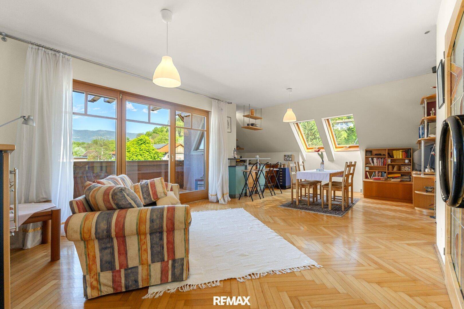 Helles Wohnzimmer im Dachgeschoss mit Parkettboden, Dachfenstern und Zugang zu einem Balkon.