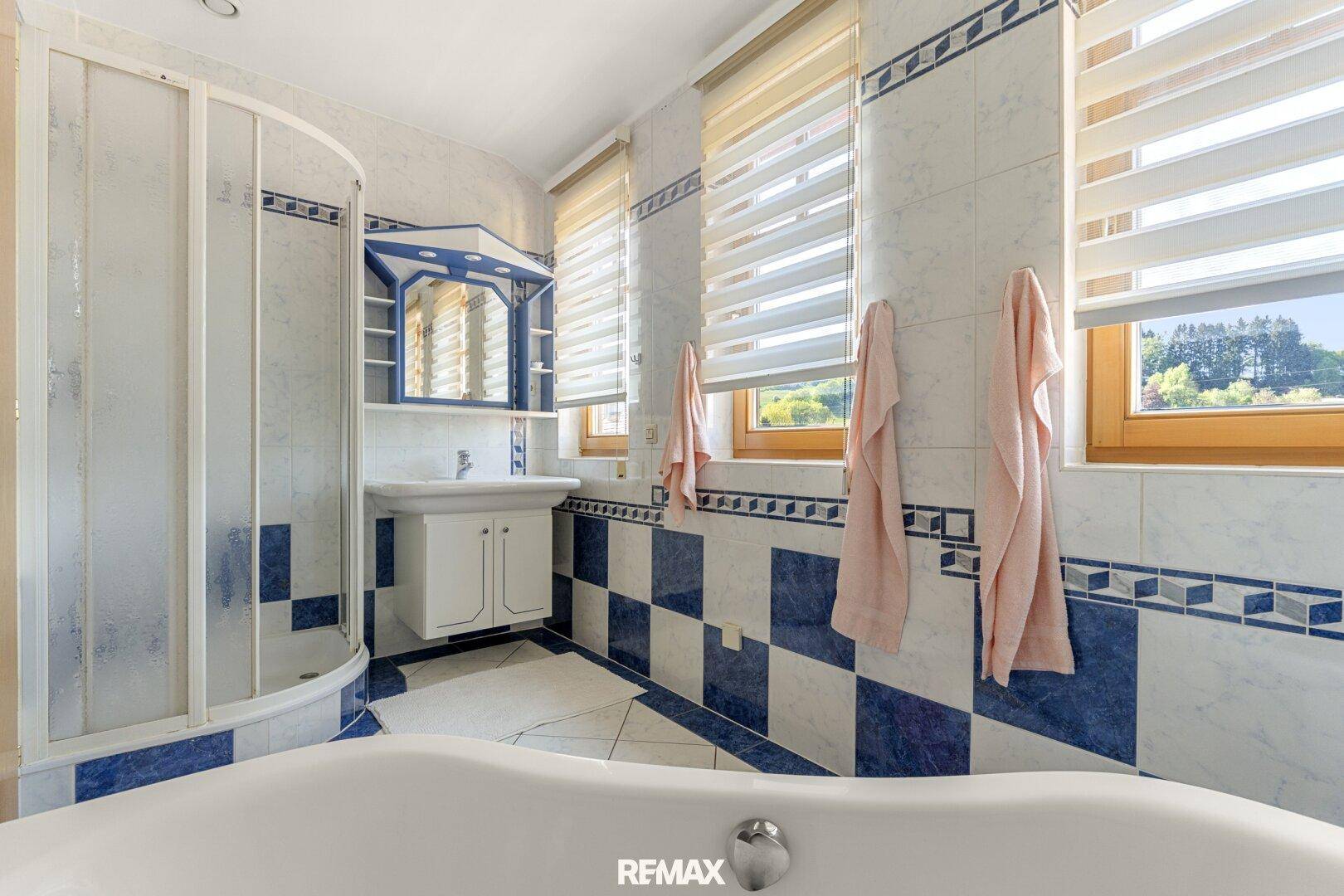 Badezimmer mit auffälligen blau-weißen Fliesen, Duschkabine und Badewanne, hell durch Fenster.