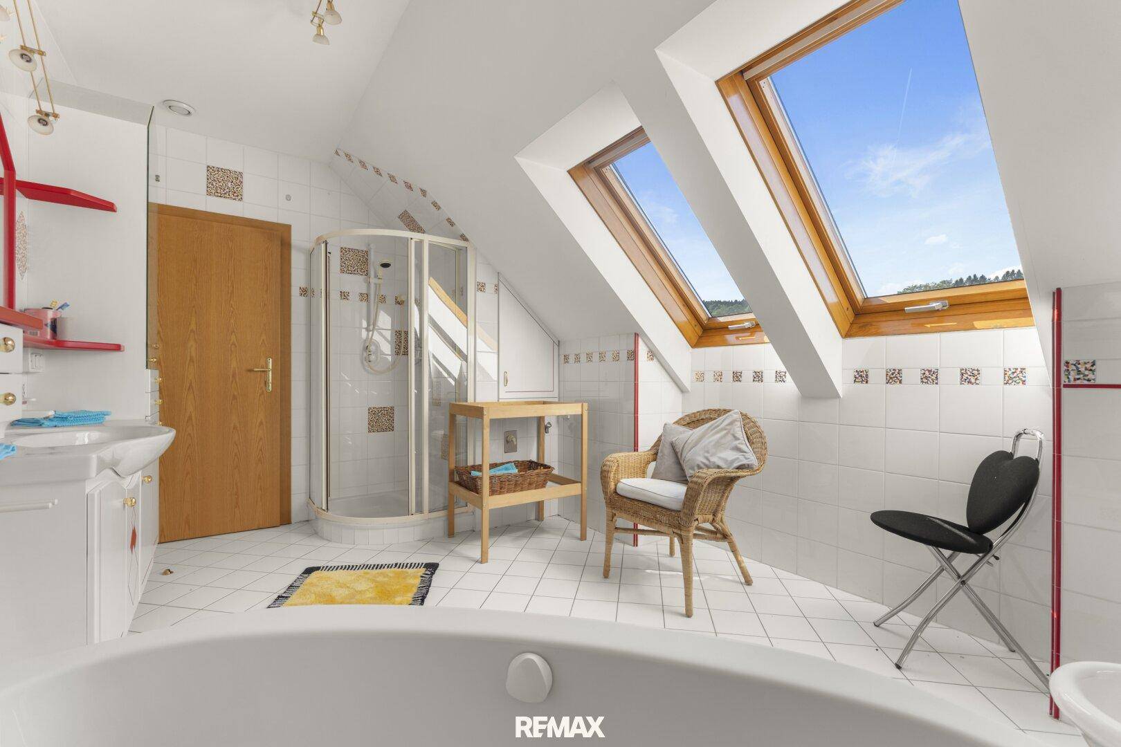 Helles Dachgeschoss-Badezimmer mit Dachfenstern, weißen Fliesen, Duschkabine und Badewanne.