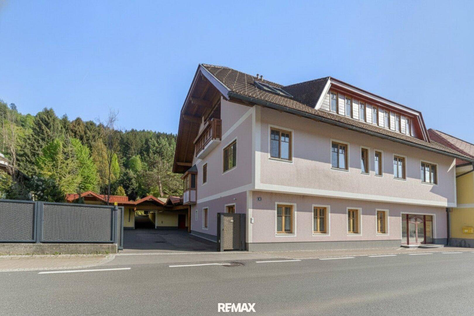 Ansicht der Gebäudefassade von der Straße aus mit mehreren Fenstern und einem Carport im Hintergrund.