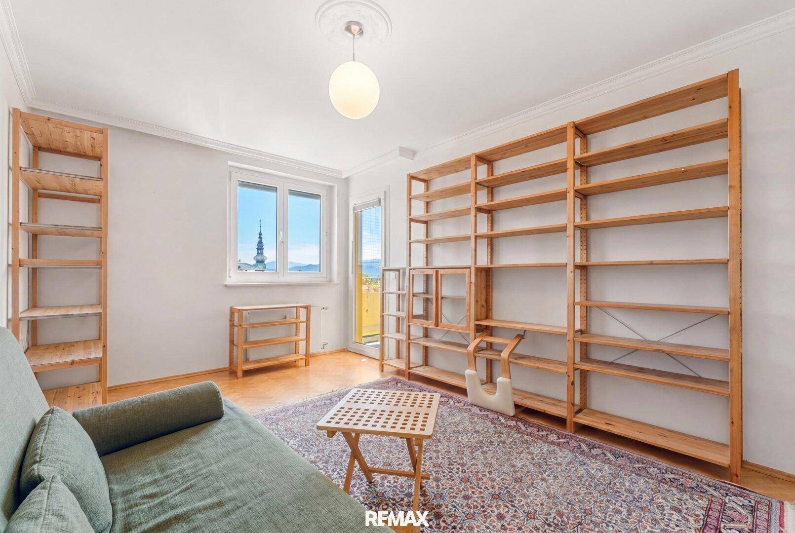 Heller Raum mit Holzbücherregalen, Sofa und Blick auf einen Kirchturm.