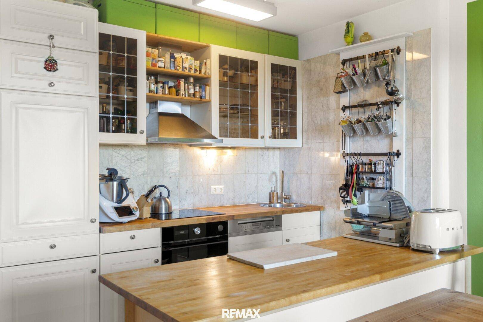 Funktionale Küche mit weißen Schränken, Holz-Arbeitsplatten und grüner Akzentwand.