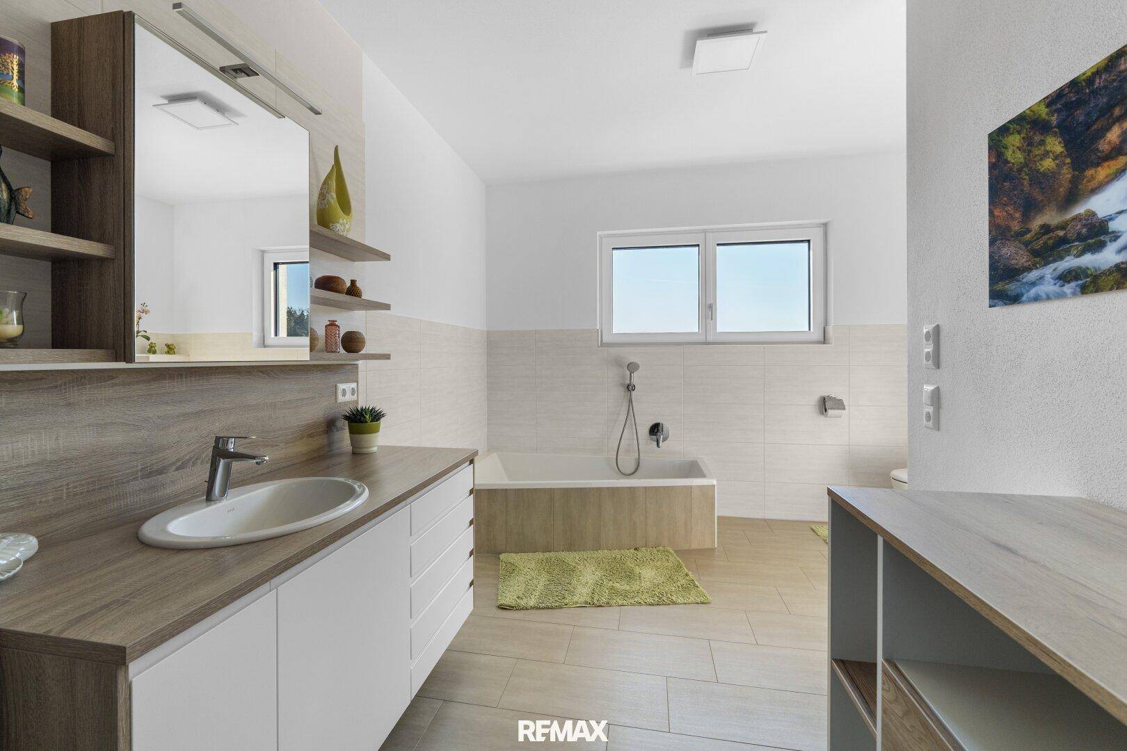 Modernes Badezimmer mit Badewanne, Einzelwaschbecken und Fenster, hell gefliest.