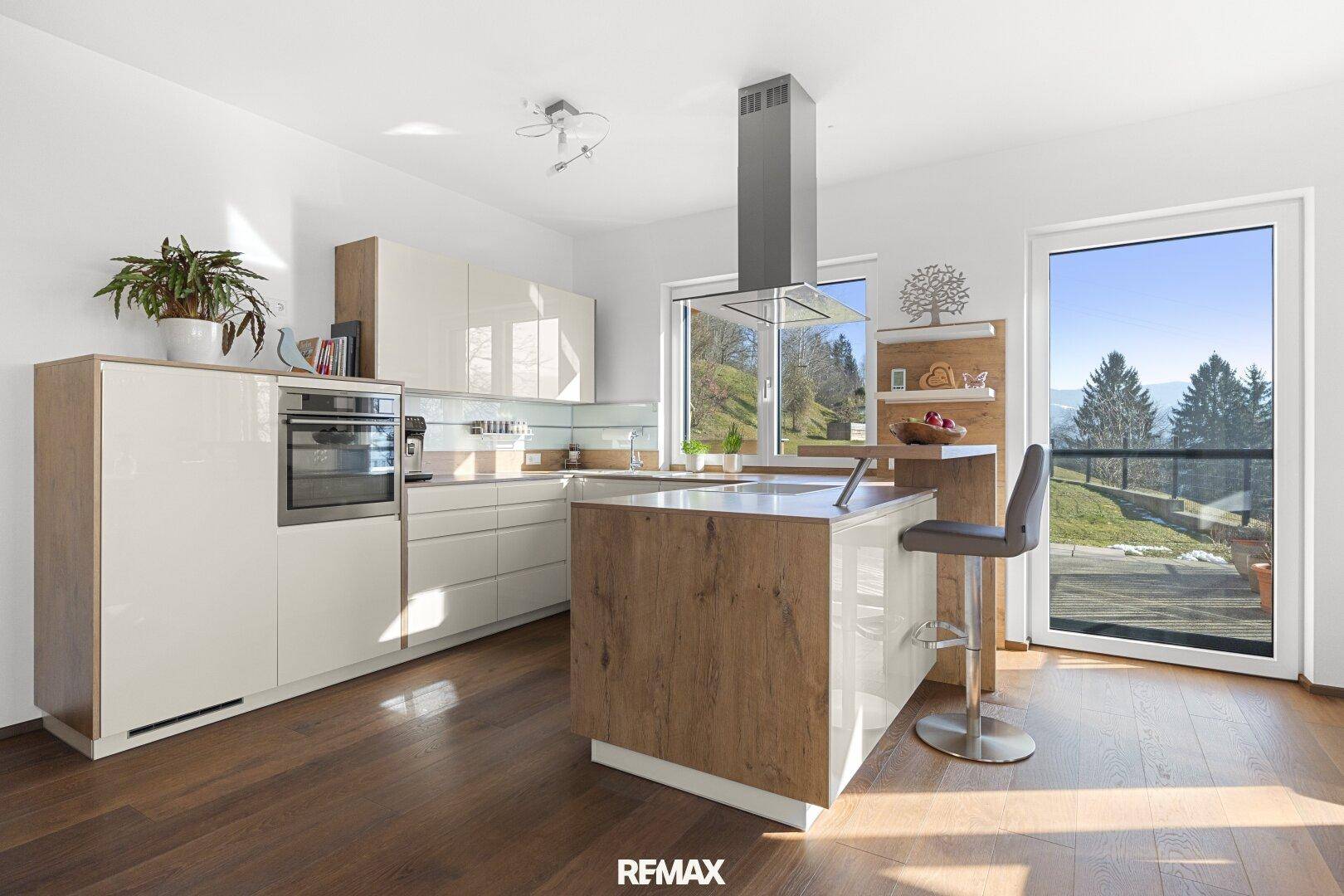 Moderne Küche mit Kochinsel, integriertem Backofen und Zugang zu einem Balkon mit Bergblick.
