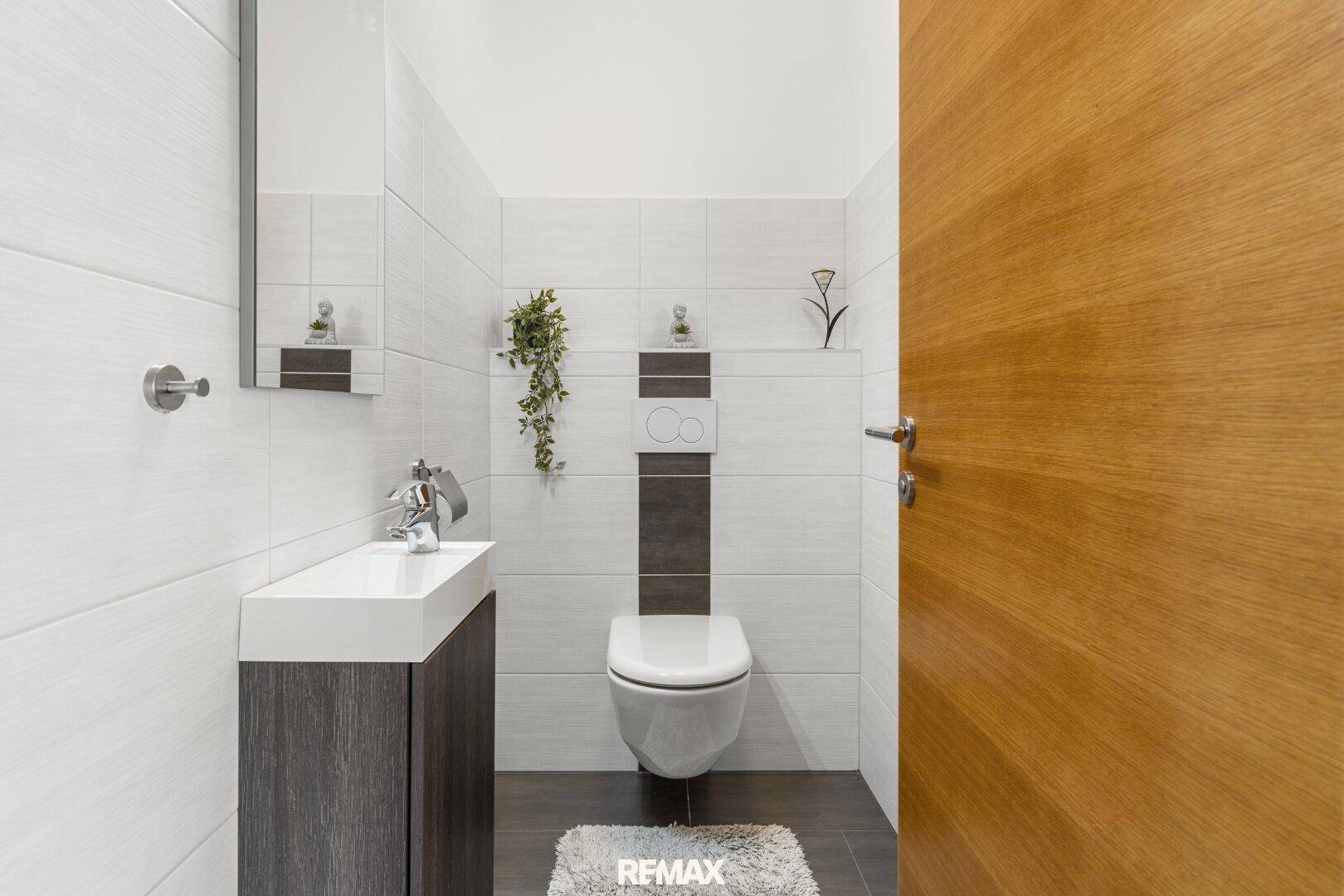 Modernes Gäste-WC mit wandhängender Toilette und kleinem Waschbecken, in eleganten Grau- und Weißtönen.