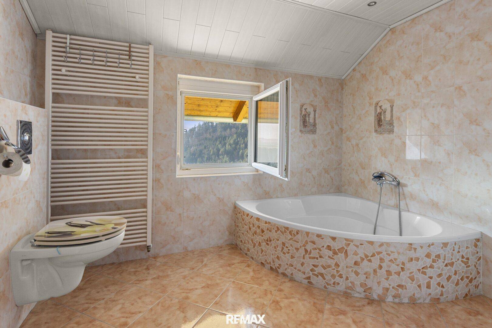 Helles Badezimmer mit Eckbadewanne, WC und beheiztem Handtuchhalter, mit Bergblick.
