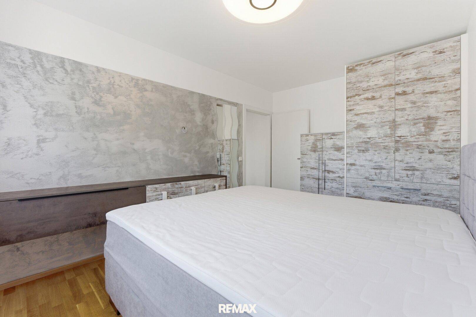 Schlafzimmer mit modernem Boxspringbett, Holzboden und dekorativer Wandgestaltung.