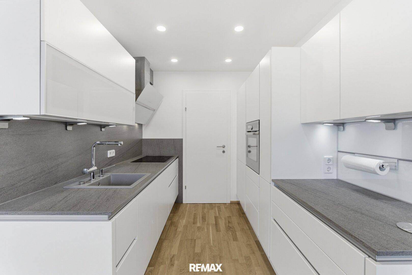 Moderne, helle Küche mit weißen Schränken, grauen Arbeitsplatten und Holzboden.