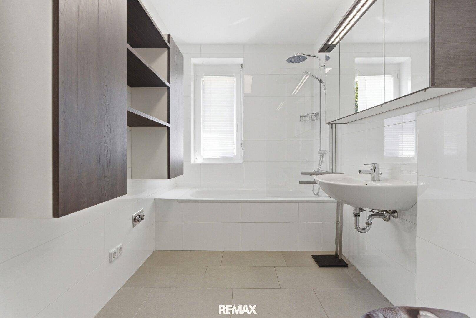 Modernes Badezimmer mit Badewanne, Dusche, Waschbecken und Fenster für Tageslicht.