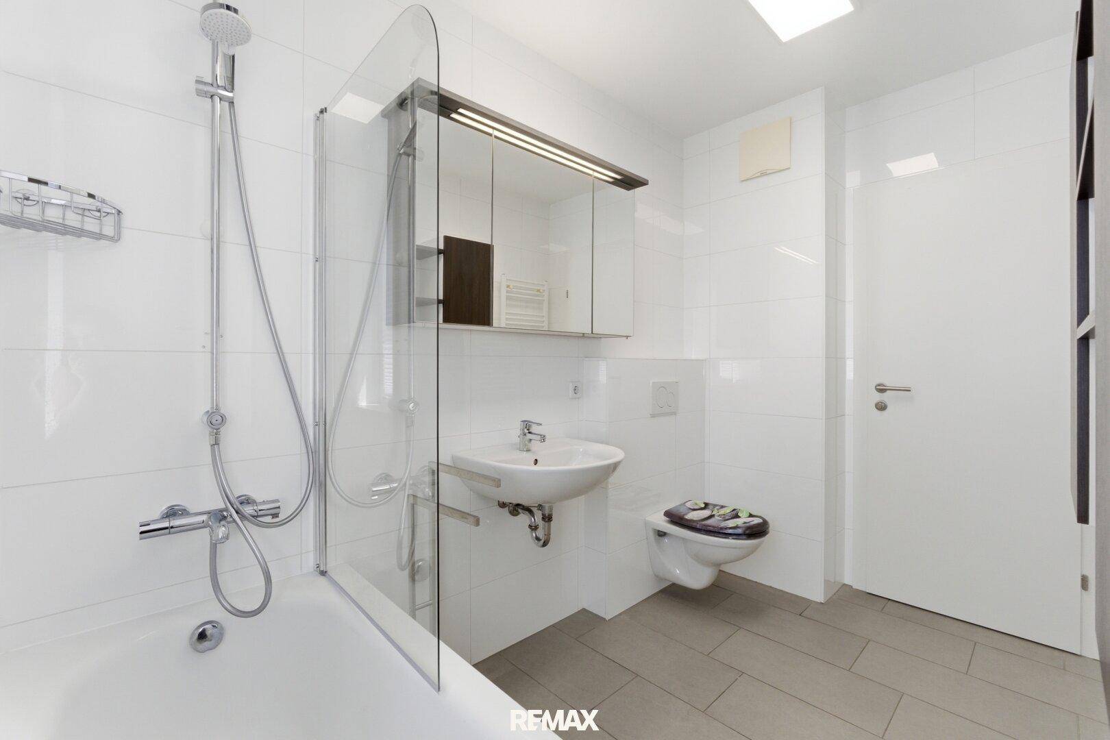 Helles Badezimmer mit Badewanne, Duschabtrennung, WC und modernem Waschbecken.