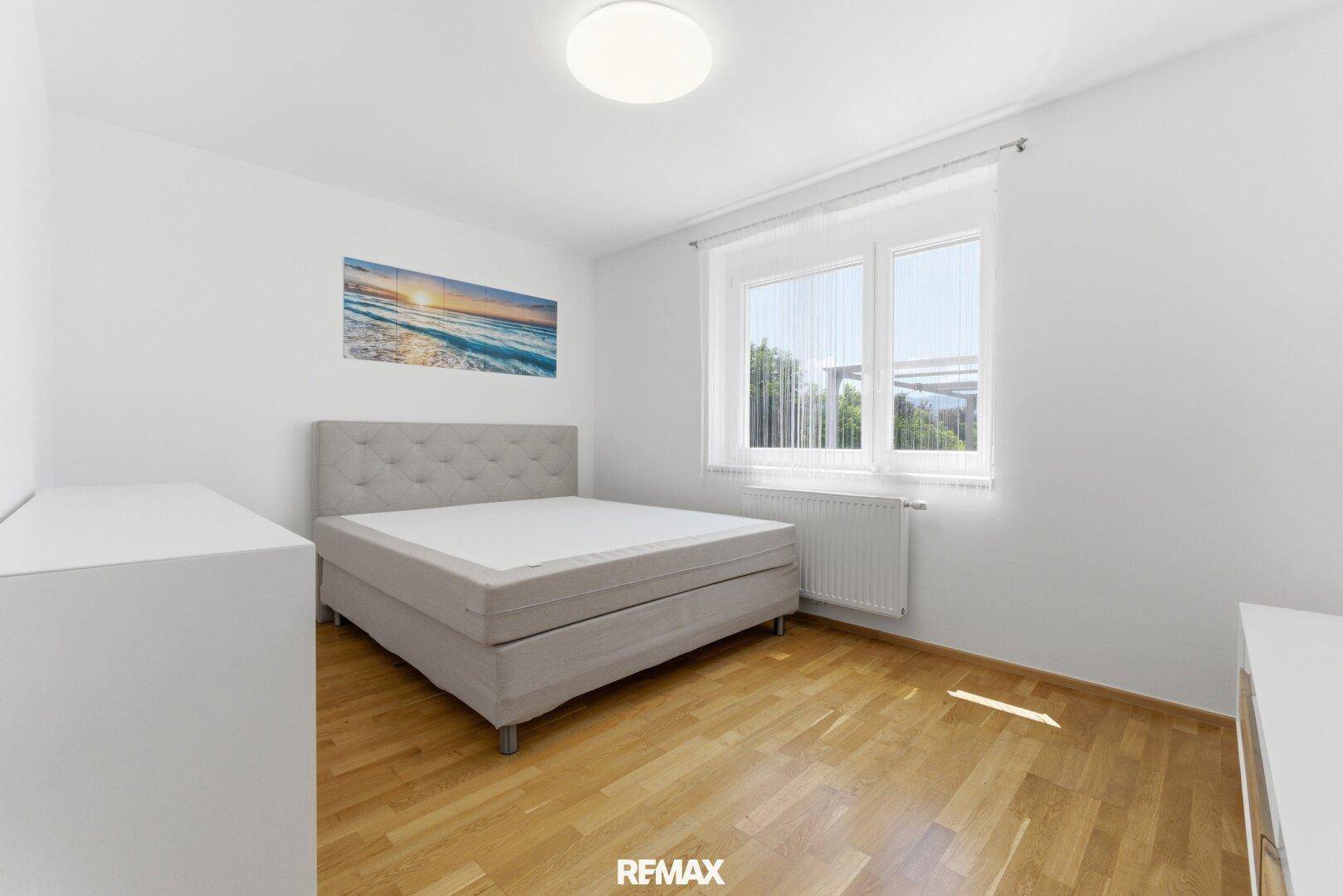 Freundliches Schlafzimmer mit Holzboden, großem Fenster und Blick auf die Umgebung.