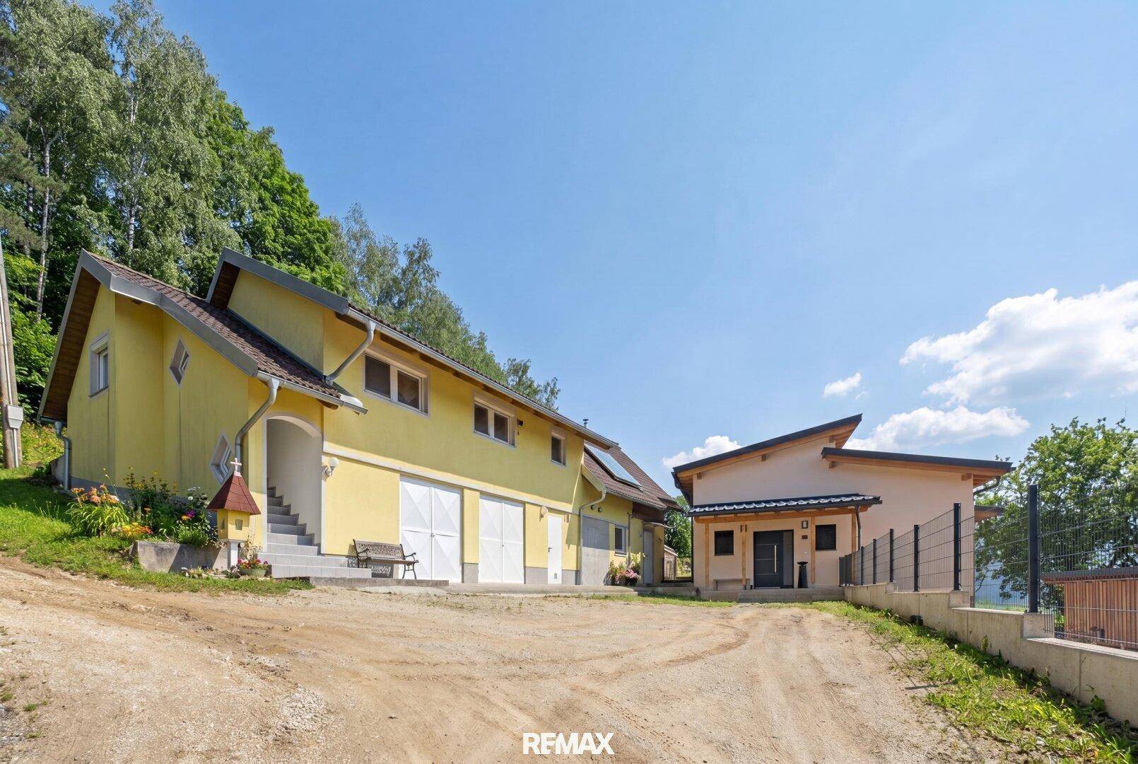 Zwei Gebäude auf einem Grundstück mit Schotterzufahrt, darunter ein gelbes Haus mit Garagen.