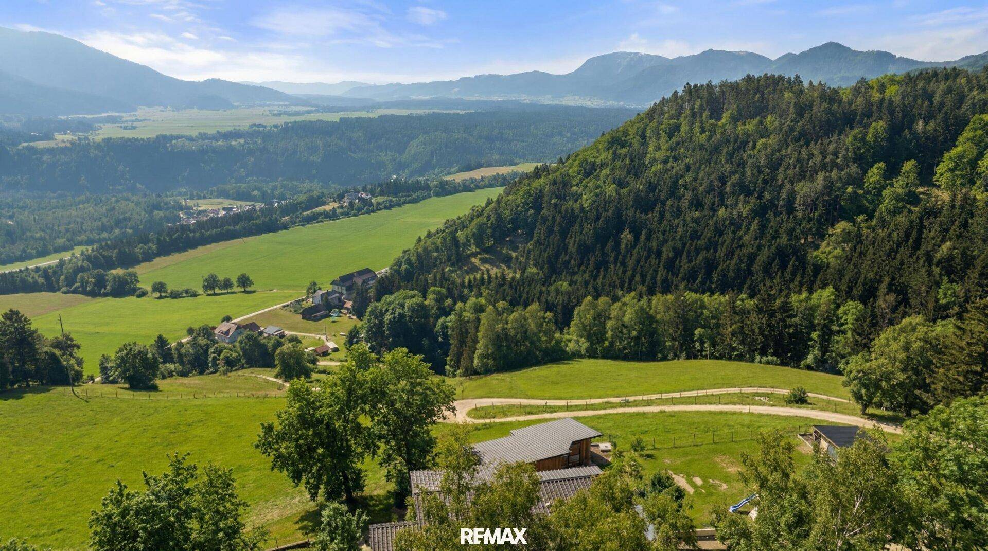 Malerische Luftaufnahme eines Anwesens in einem grünen Tal, umgeben von Bergen und Wäldern.