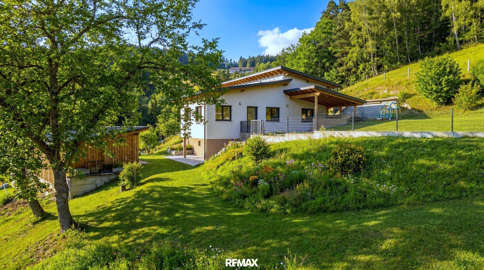Haus auf einem grünen Hügelgrundstück mit weitläufigem Garten und altem Baumbestand.