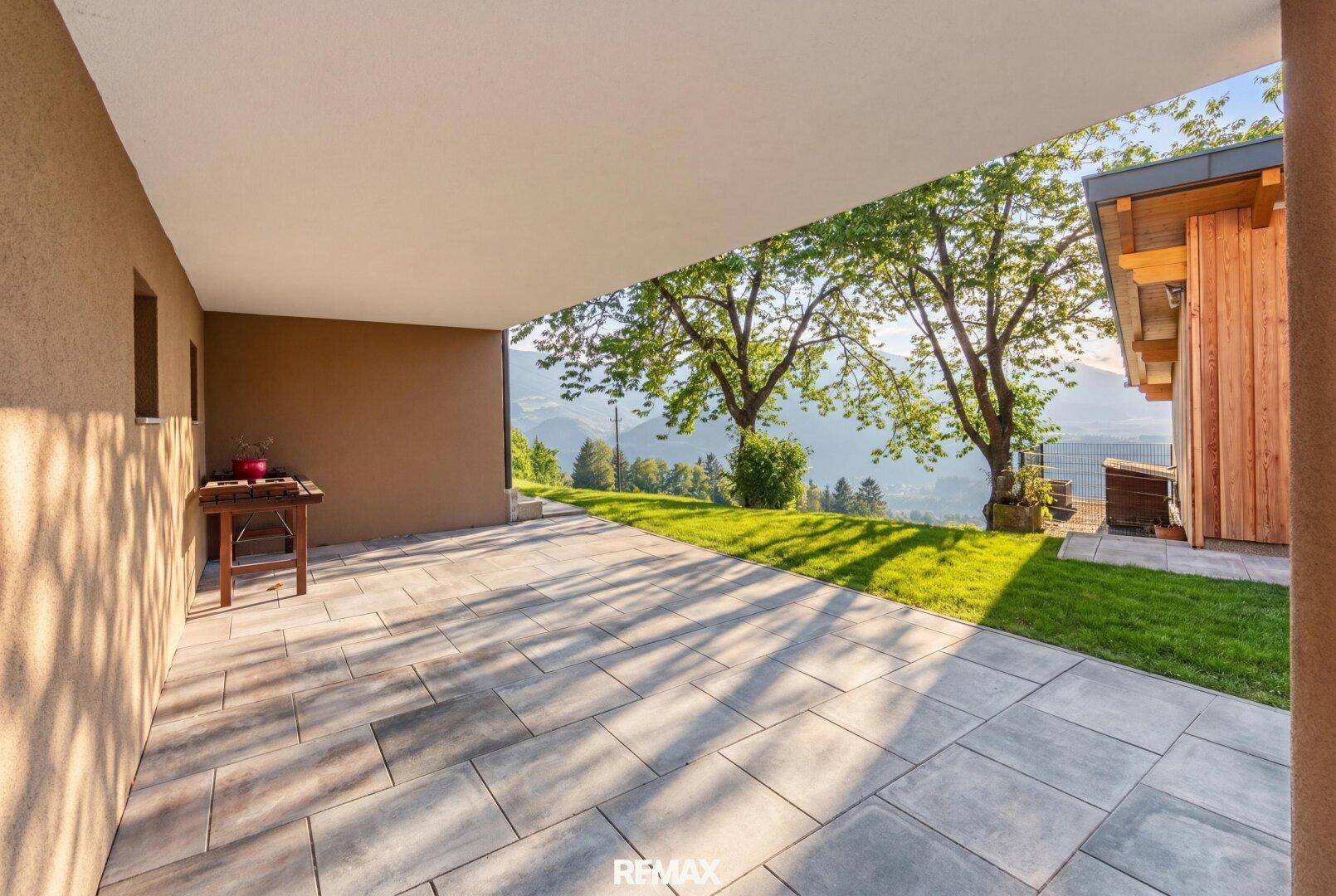 Überdachte Terrasse mit Fliesenboden und Grillbereich, bietet einen weiten Blick auf die grüne Landschaft.