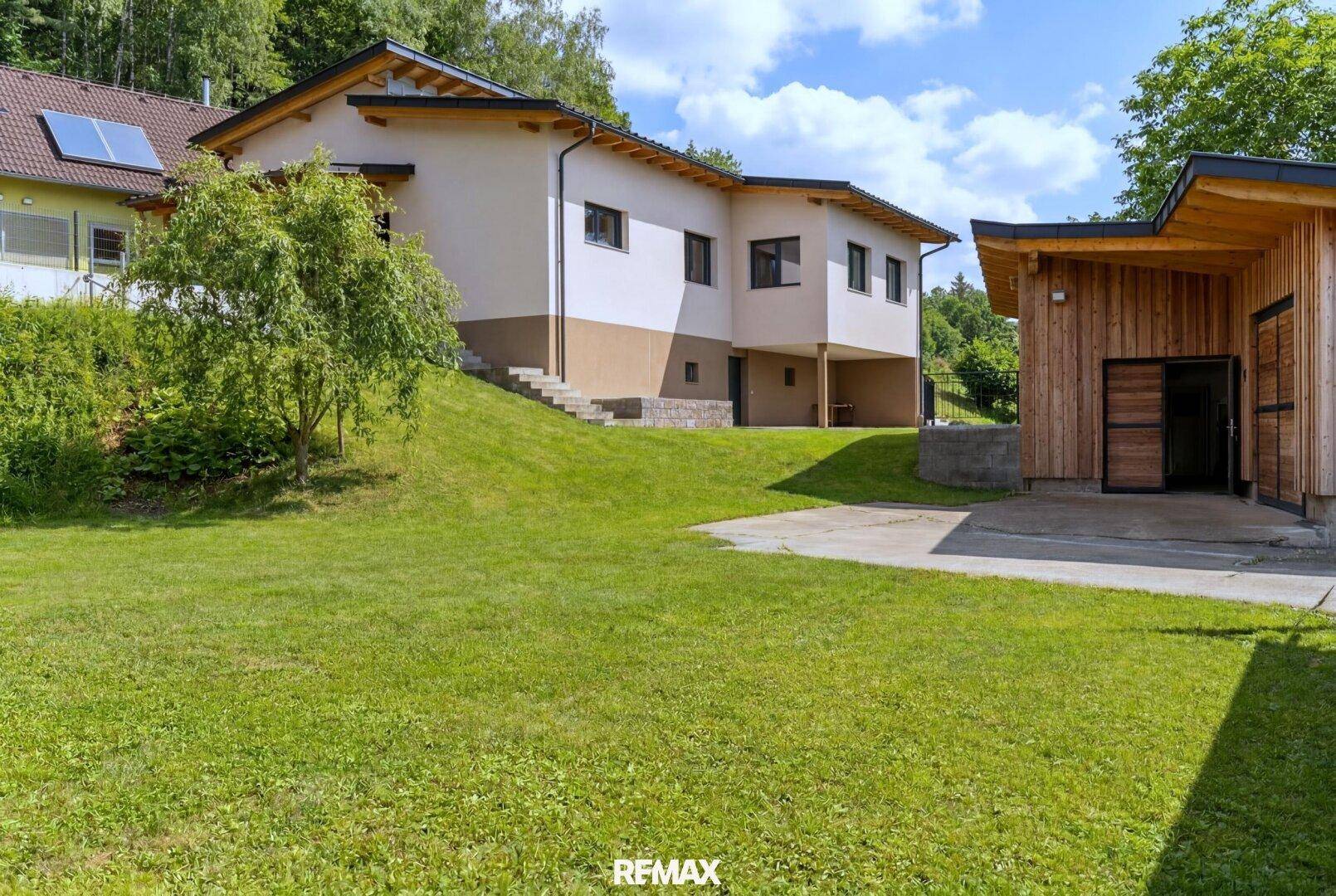 Weitläufiges Grundstück mit Wohnhaus und separatem Holzgebäude auf einer grünen Wiese.