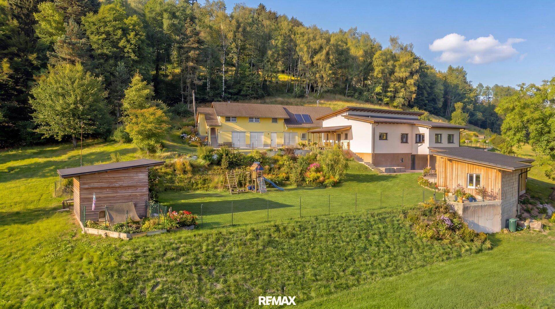 Luftaufnahme eines weitläufigen Anwesens mit mehreren Gebäuden, großem Garten und umgebender Natur.