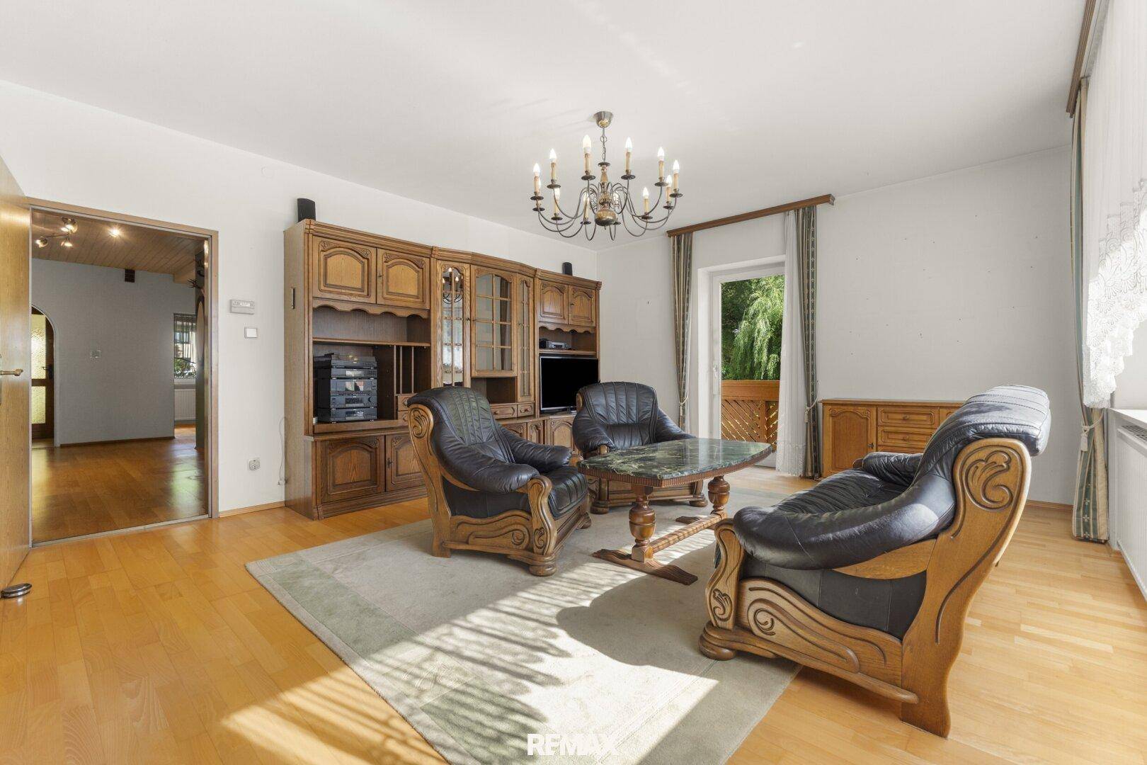 Traditionelles Wohnzimmer mit klassischen Holzmöbeln, Ledersesseln und Zugang zum Balkon.