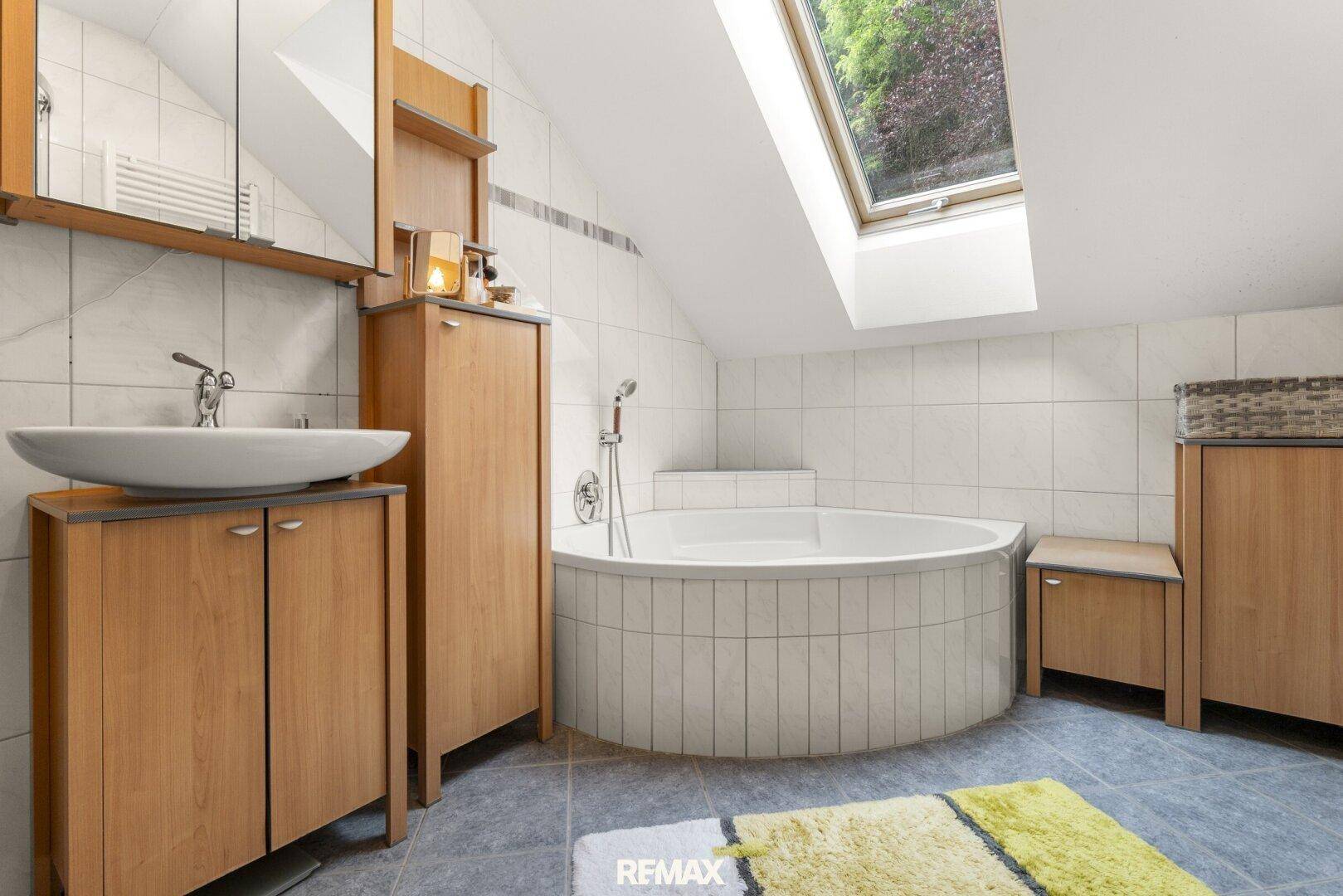 Badezimmer im Dachgeschoss mit Eckbadewanne, Einzelwaschbecken und einem Dachfenster.