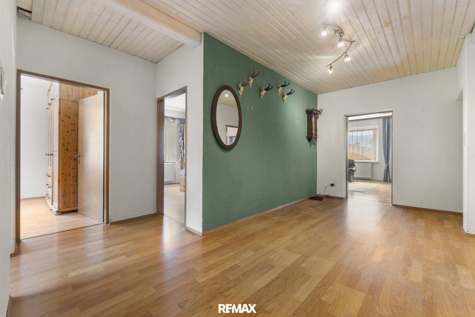 Geräumiger Flur mit Holzparkett, grüner Akzentwand und rustikalen Deckenpaneelen.