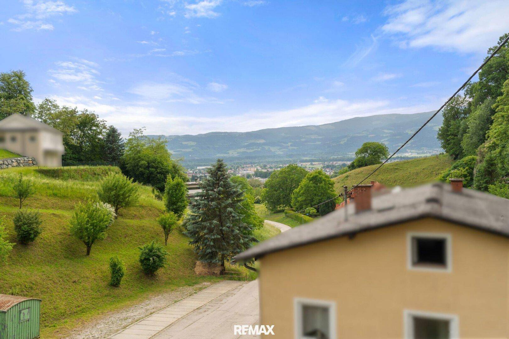 Weitläufiger Blick über die hügelige, grüne Landschaft mit einem Haus im Vordergrund.