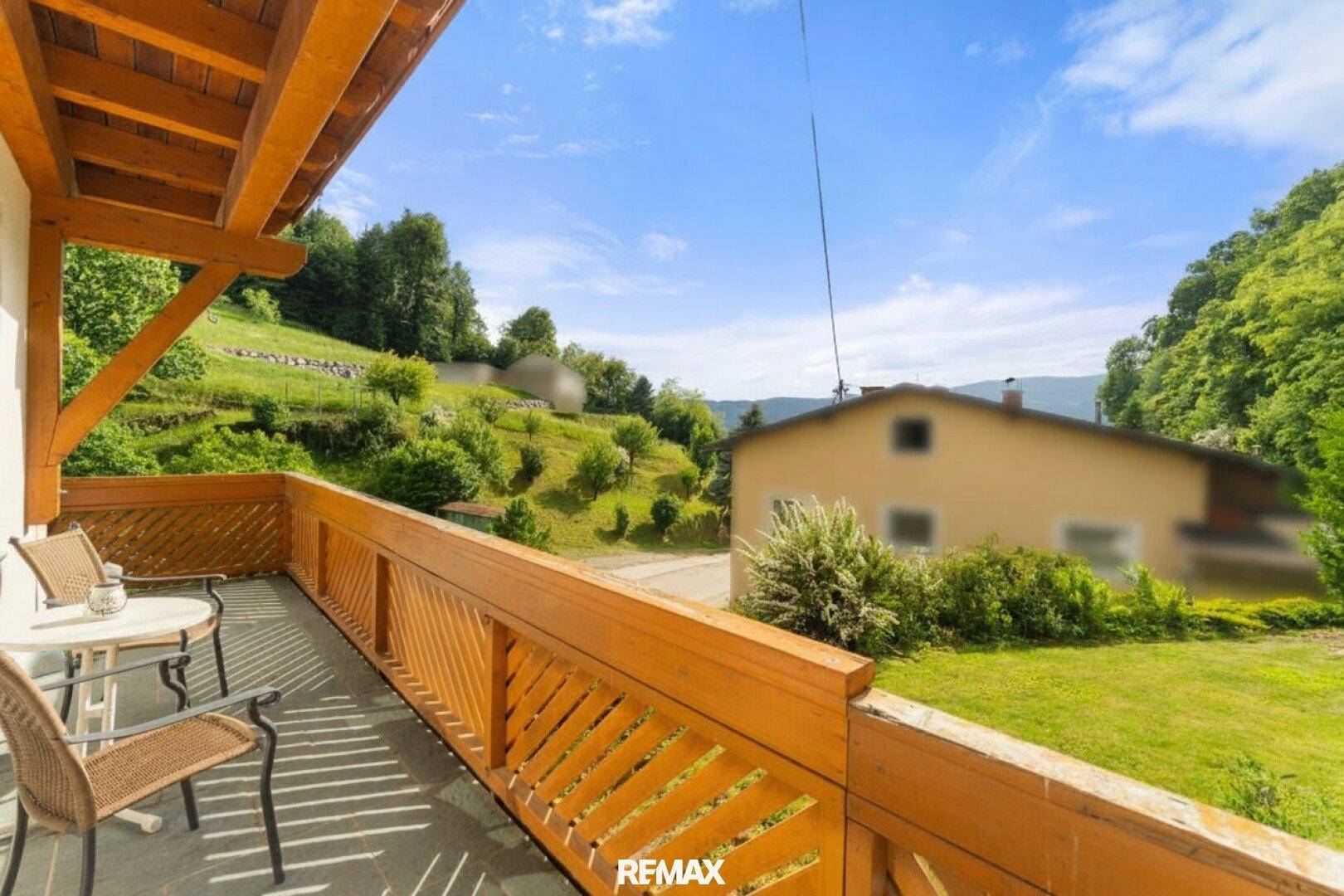 Sonniger Balkon mit Holzbalkonmöbeln und weitem Blick über die grüne Landschaft.