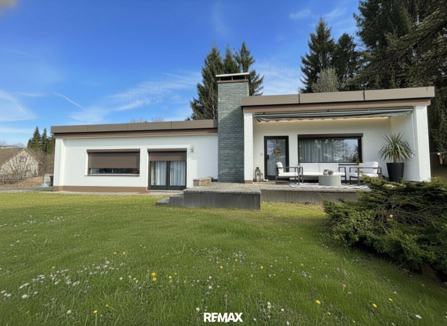 Ansicht des Hauses mit einer möblierten Terrasse und großen Fenstern, umgeben von Grünflächen.
