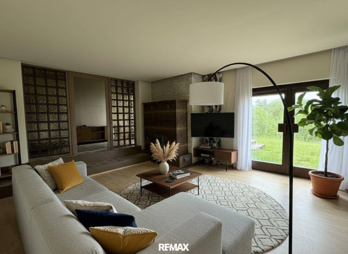 Modern eingerichtetes Wohnzimmer mit bequemer Couch, Holzboden und Blick in den Garten.