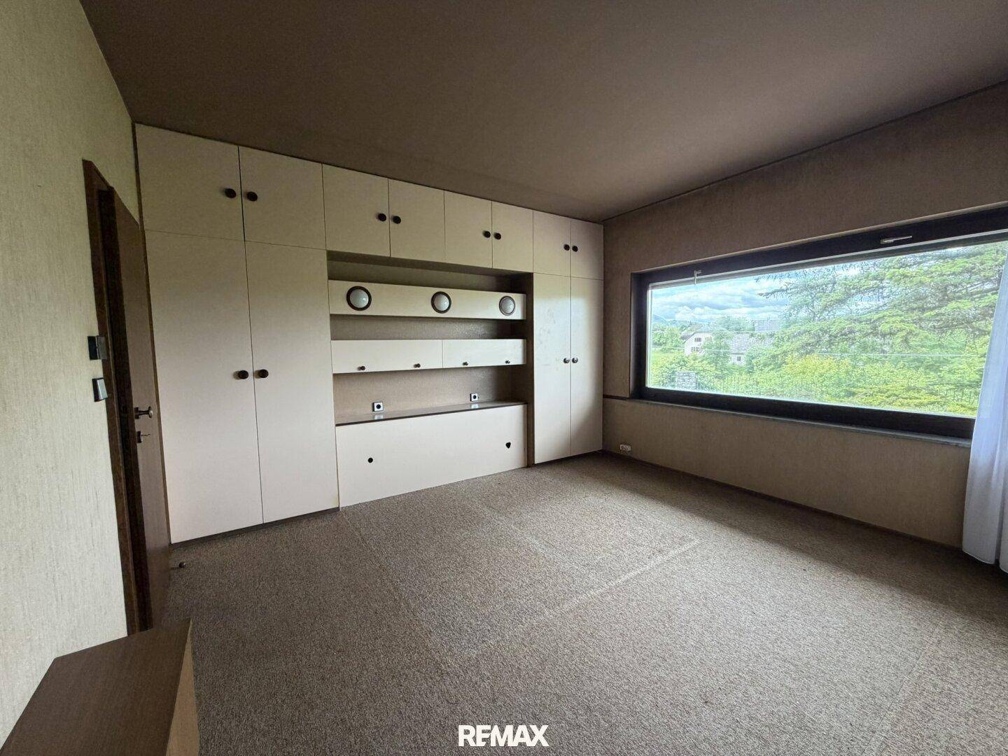Schlafzimmer mit Teppichboden, Einbauschränken und großem Fenster mit Blick ins Grüne.