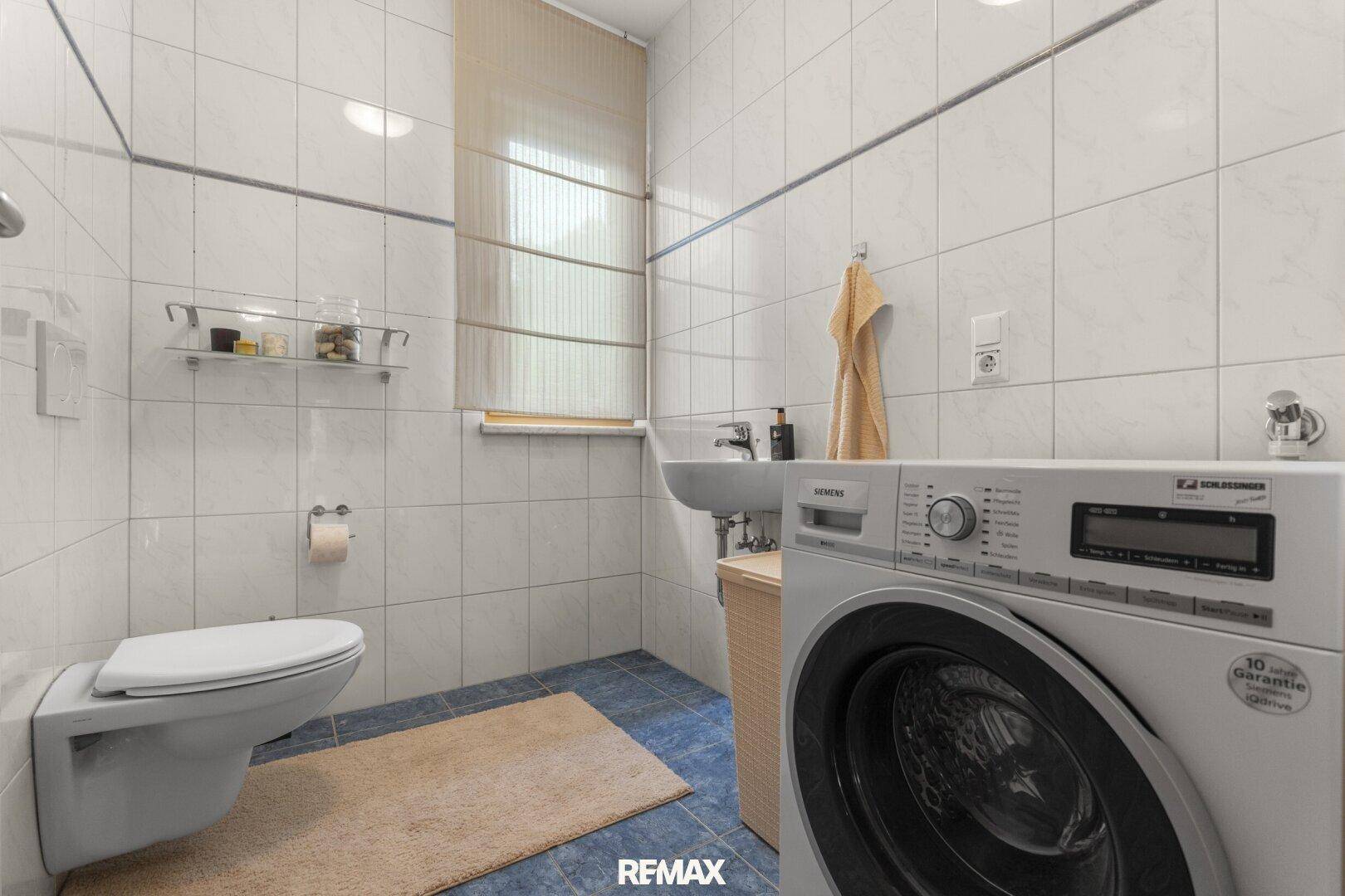 Gefliestes Badezimmer mit WC, Waschbecken und Waschmaschine, ausgestattet mit einem Fenster.