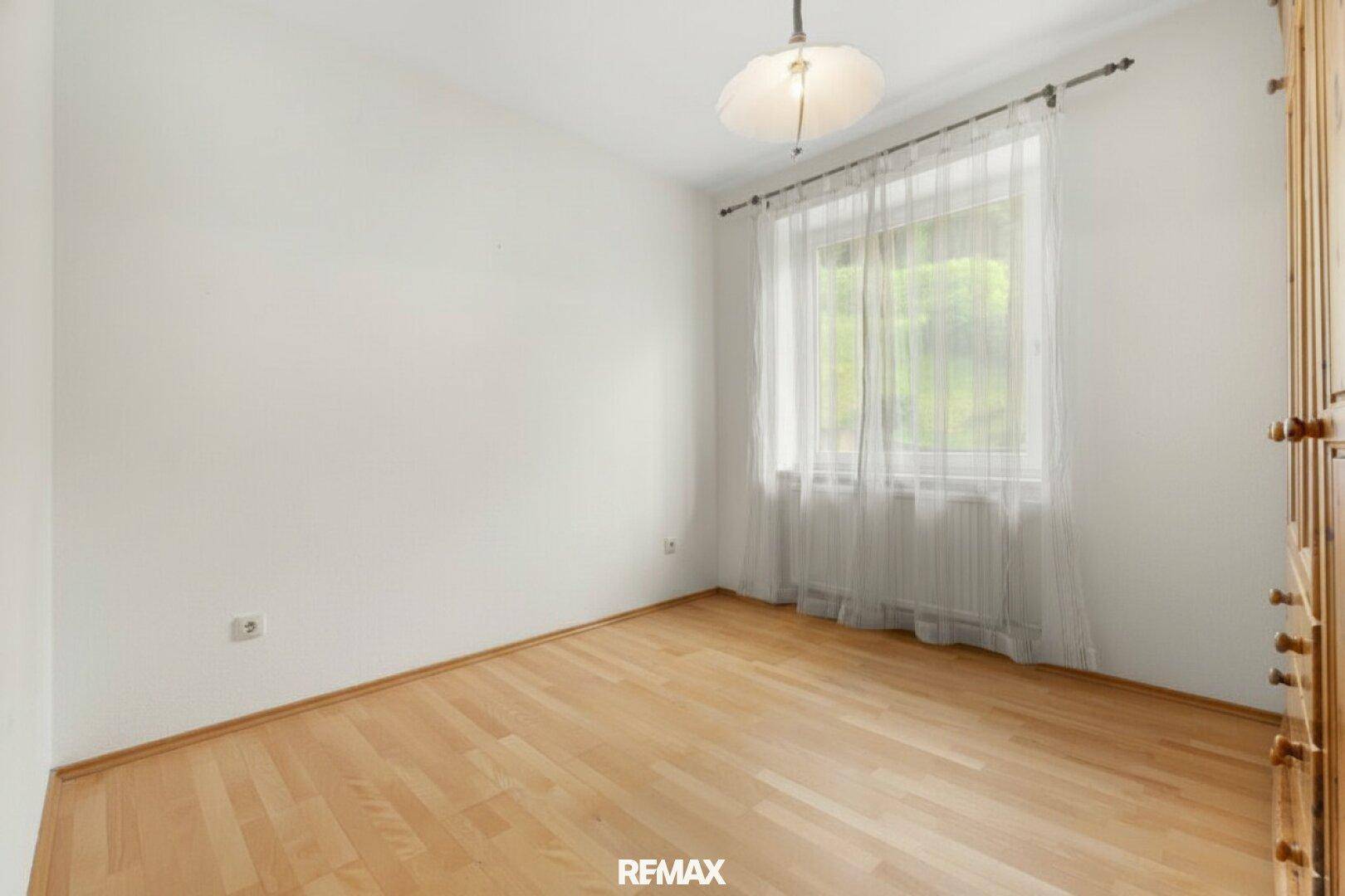 Helles, leeres Zimmer mit hellem Holzboden und einem großen Fenster, ideal als Schlafzimmer.
