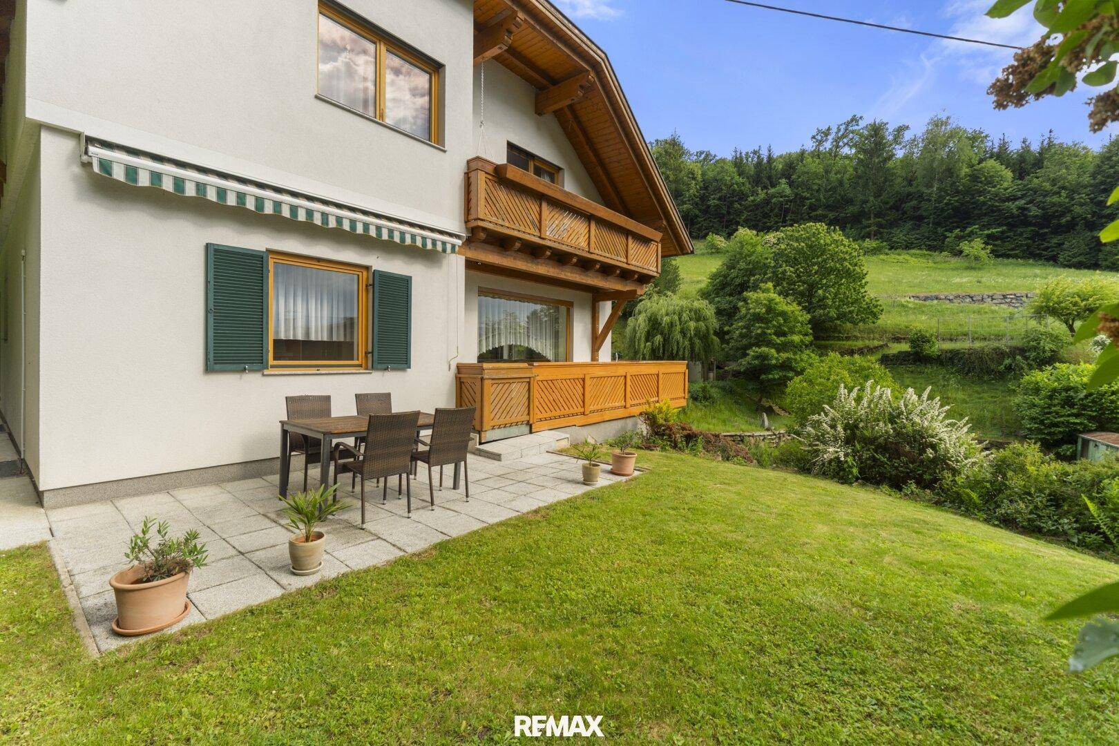 Große gepflasterte Terrasse mit Gartenmöbeln und Zugang zum Garten, umgeben von grüner Natur.