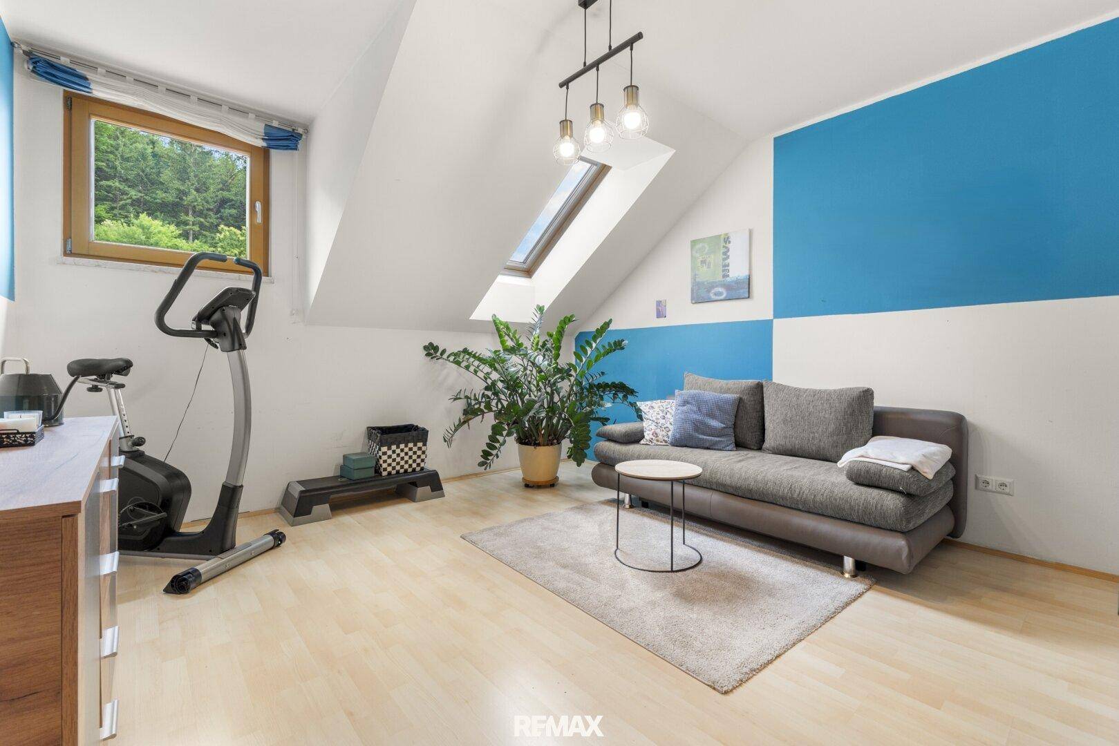Fitnessraum im Dachgeschoss mit Trainingsgerät, Sofa und einem Dachfenster für natürliches Licht.