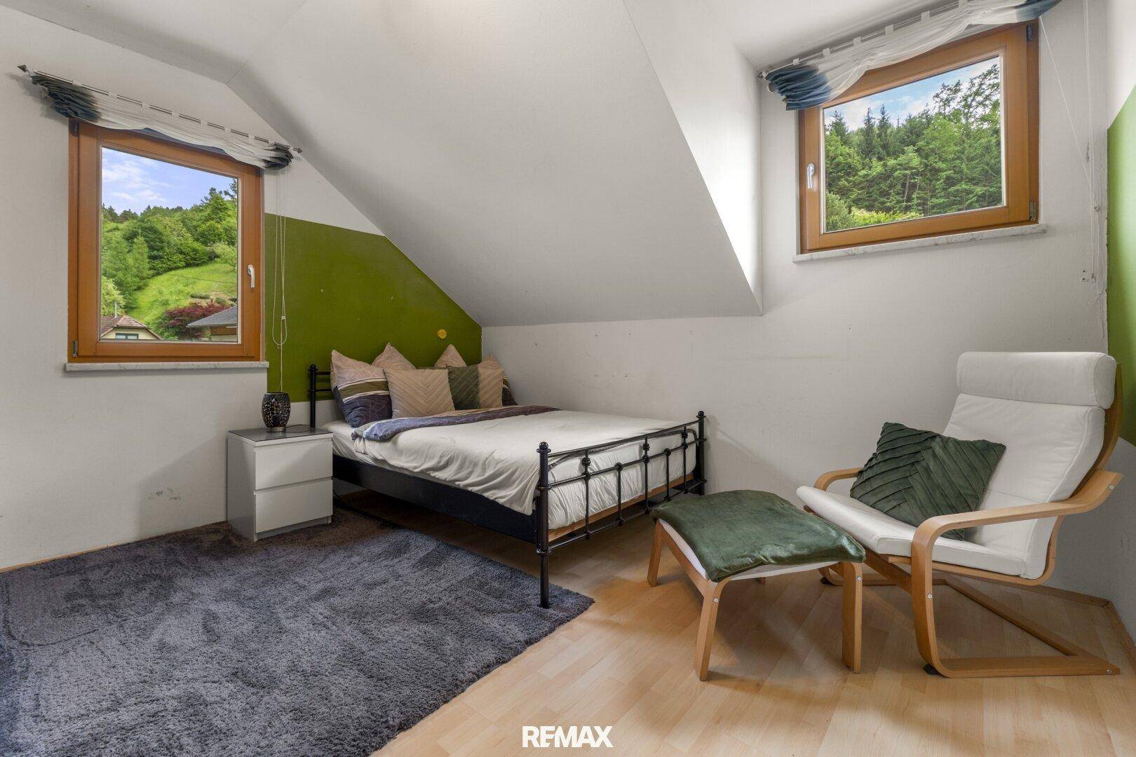 Gemütliches Schlafzimmer im Dachgeschoss mit Blick ins Grüne und einer grünen Akzentwand.