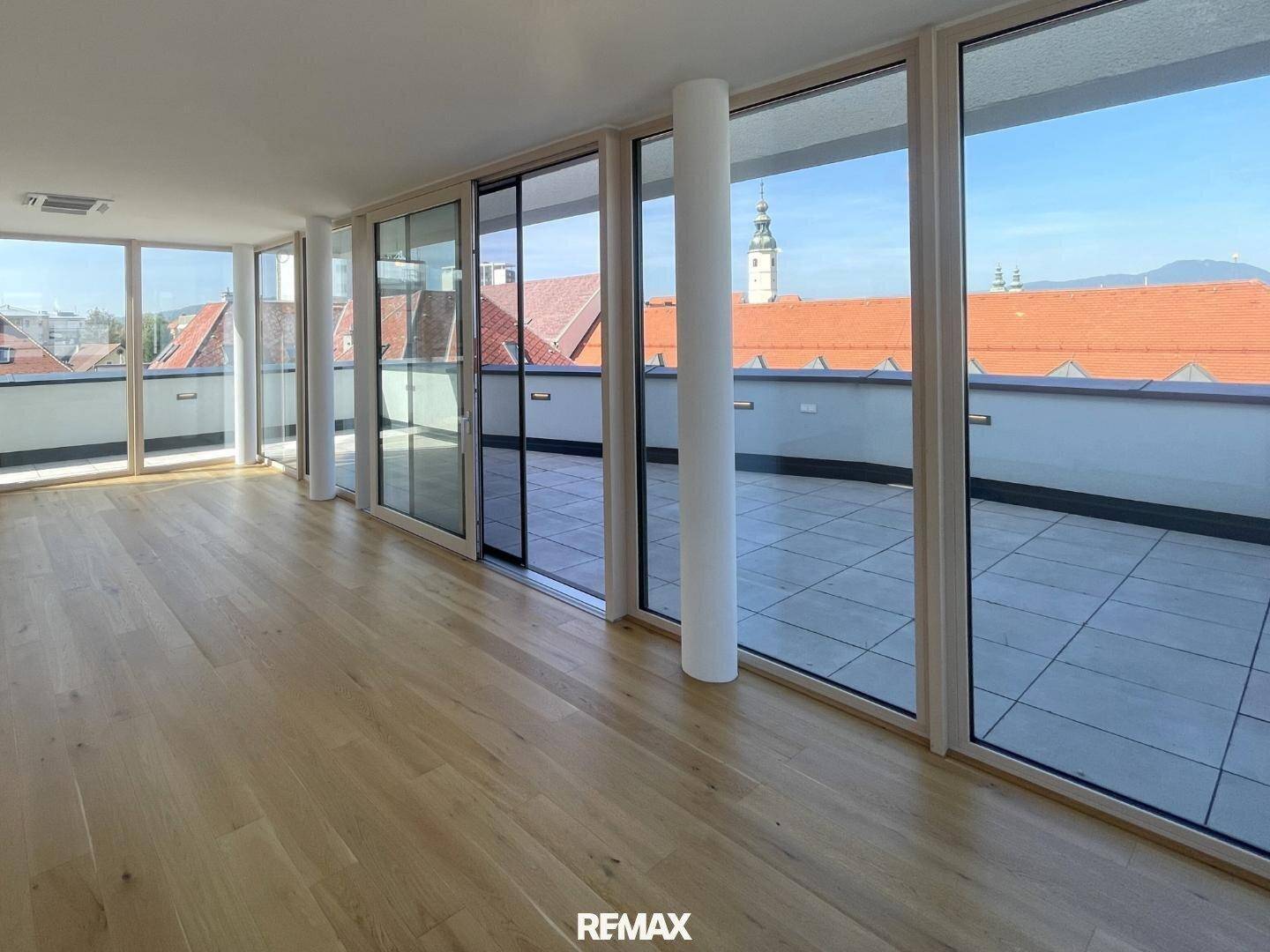 Helles Wohnzimmer mit Holzboden, großen Fenstern und Zugang zu einer weitläufigen Dachterrasse mit Stadtblick.