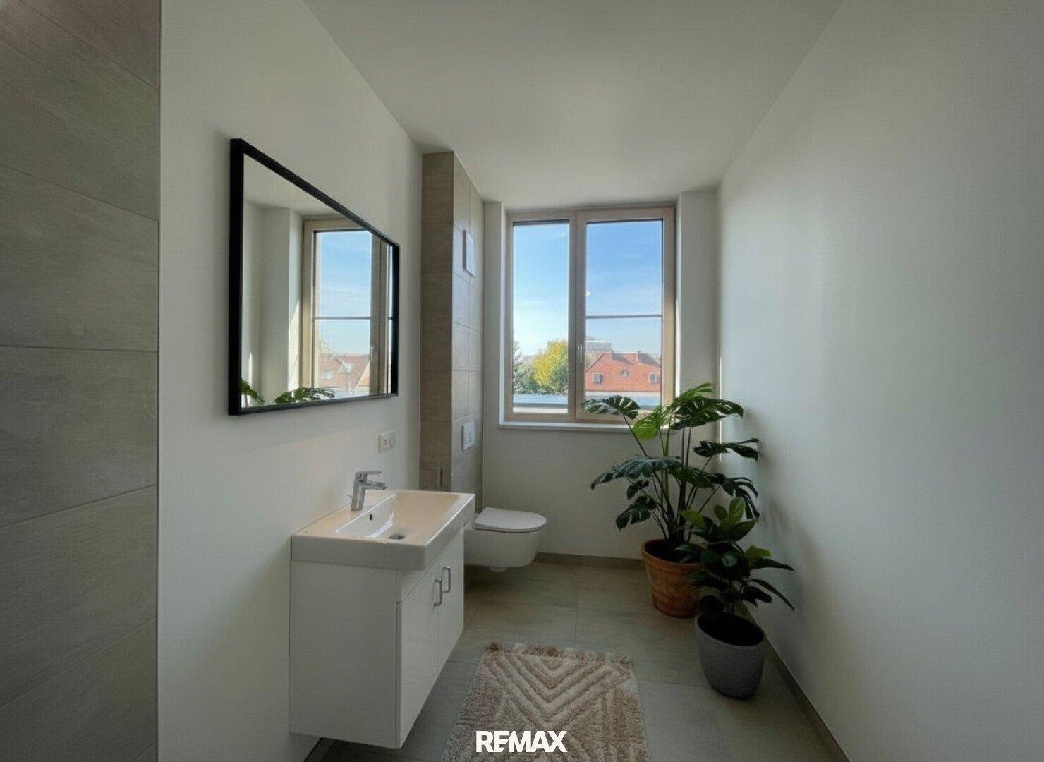 Modernes Badezimmer mit Waschtisch, wandhängendem WC, großem Spiegel und Fenster für natürliche Belichtung.