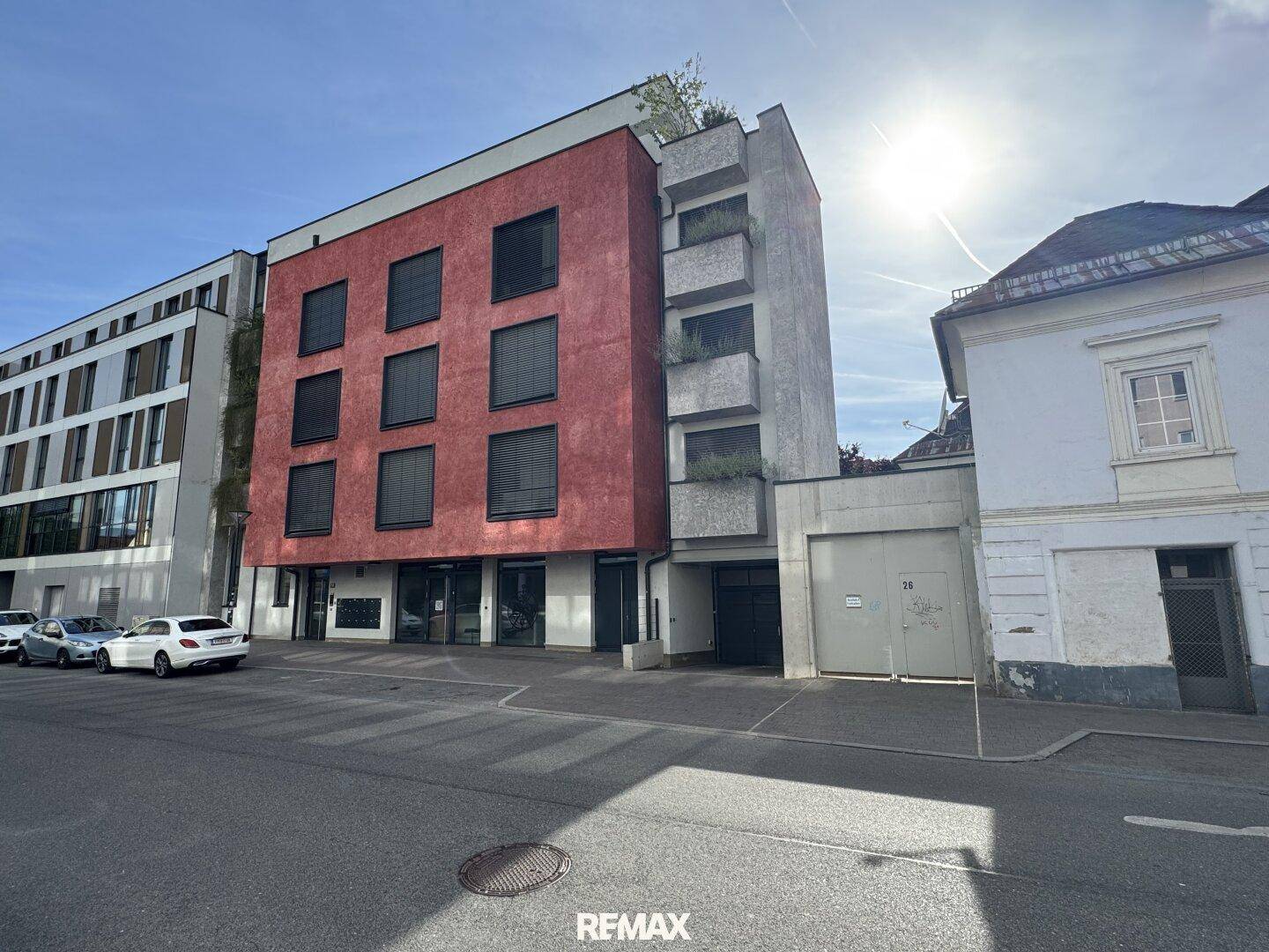 Moderne Gebäudefassade mit roter Akzentfarbe, großen Fenstern und Balkonen an einer städtischen Straße.